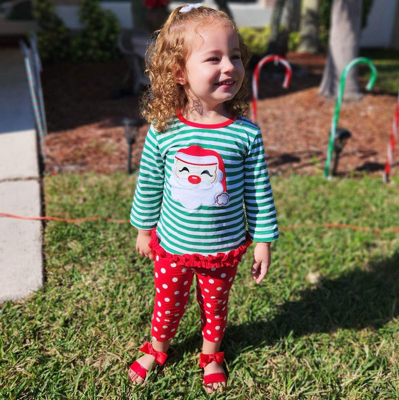 A festive girls' outfit featuring a Santa tunic top with ruffle trim and red polka dot pants, perfect for holiday celebrations.