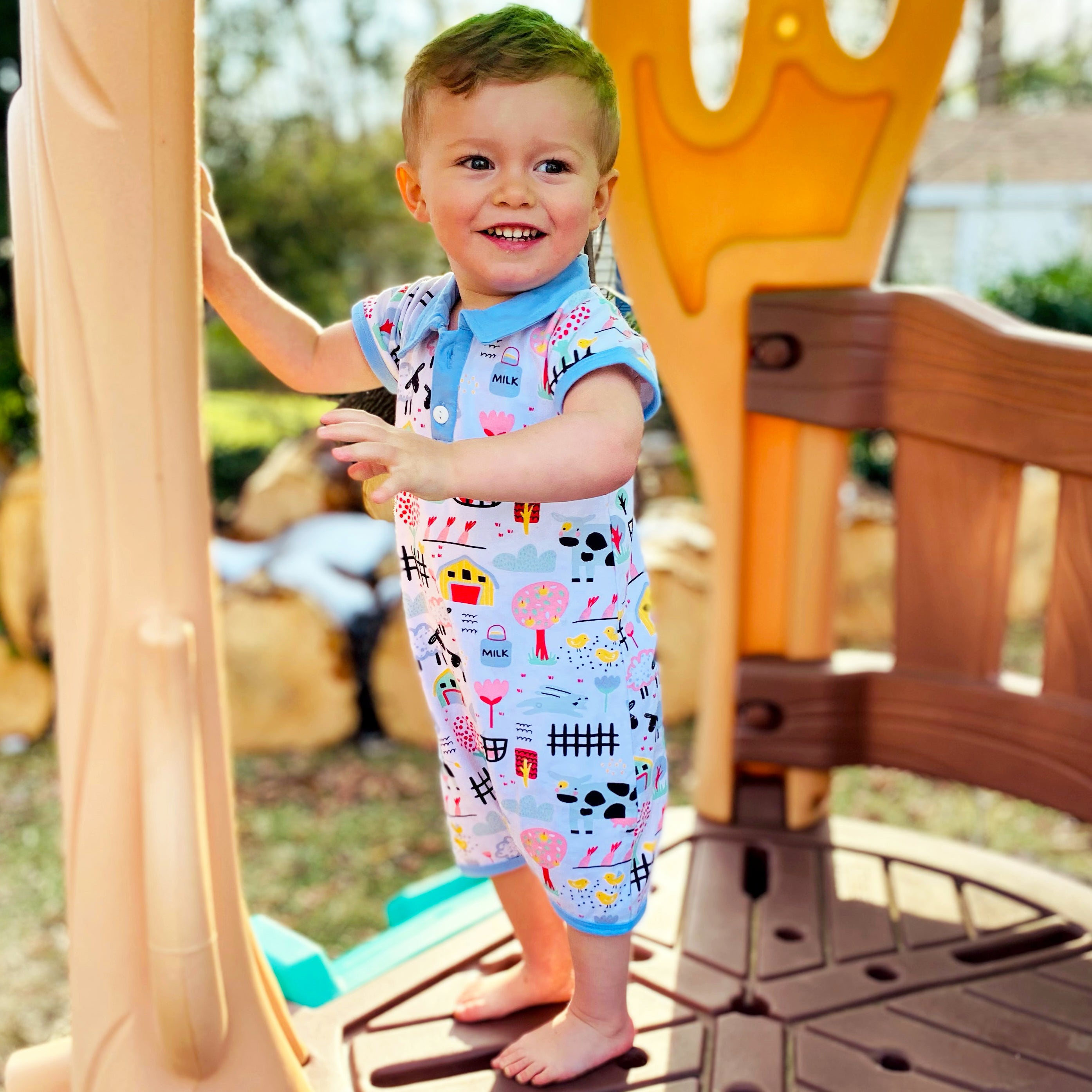 Baby boy wearing a Fun Farm Animal Romper with blue collar and buttons, featuring playful farm animal prints.