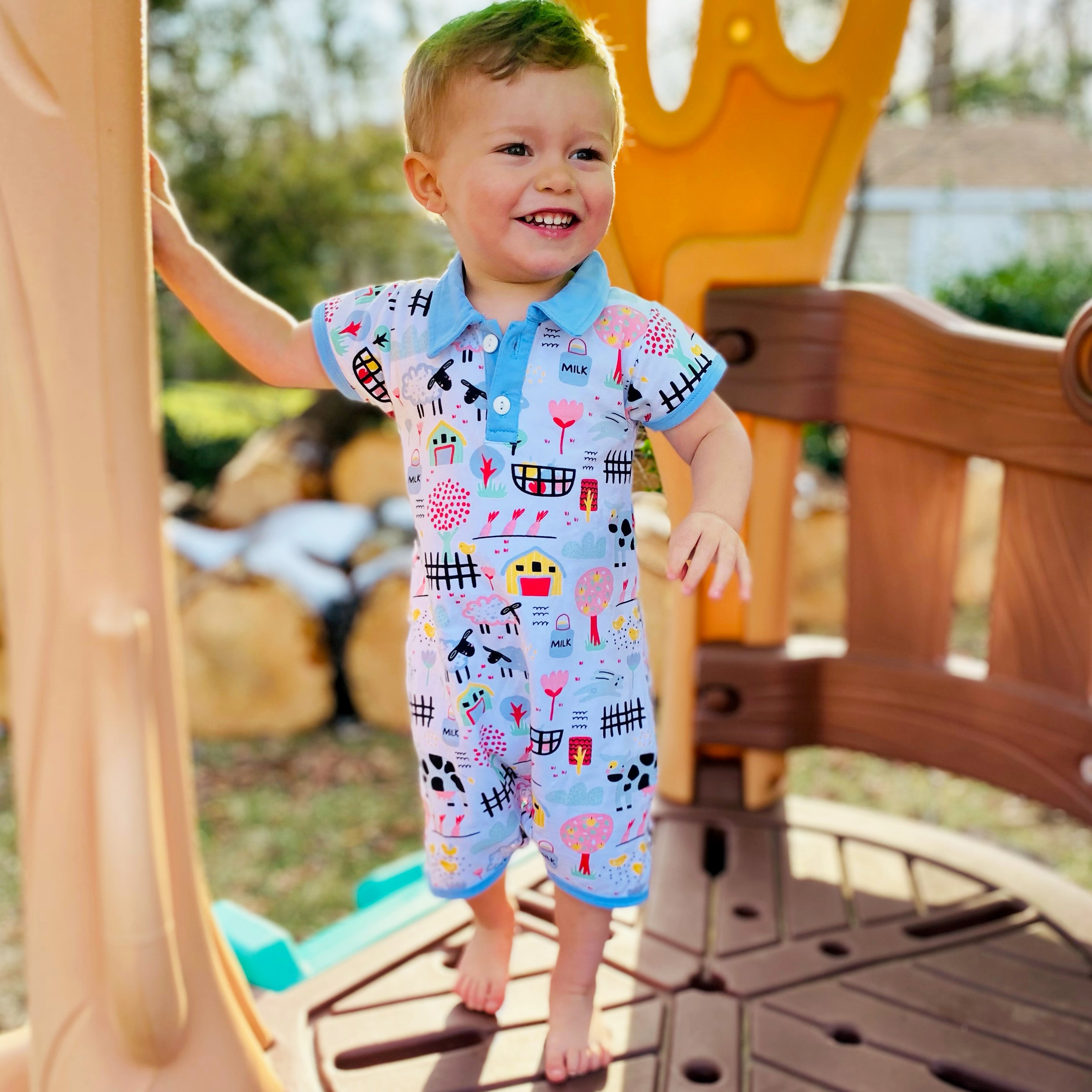 Baby boy wearing a Fun Farm Animal Romper with blue collar and buttons, featuring playful farm animal prints.