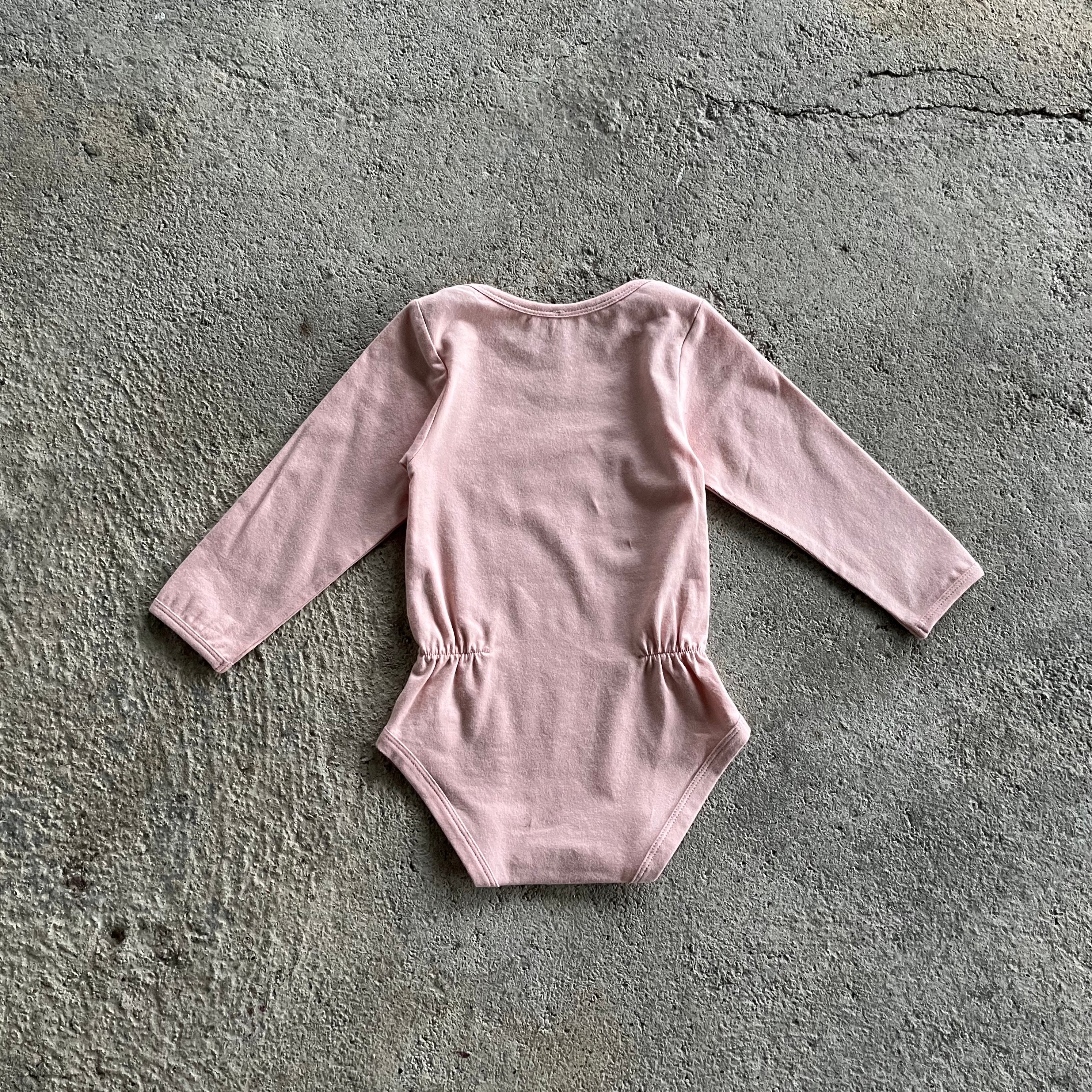 A soft pink body for babies and toddlers with elasticised waist and snap closures, made from organic cotton and elastane.