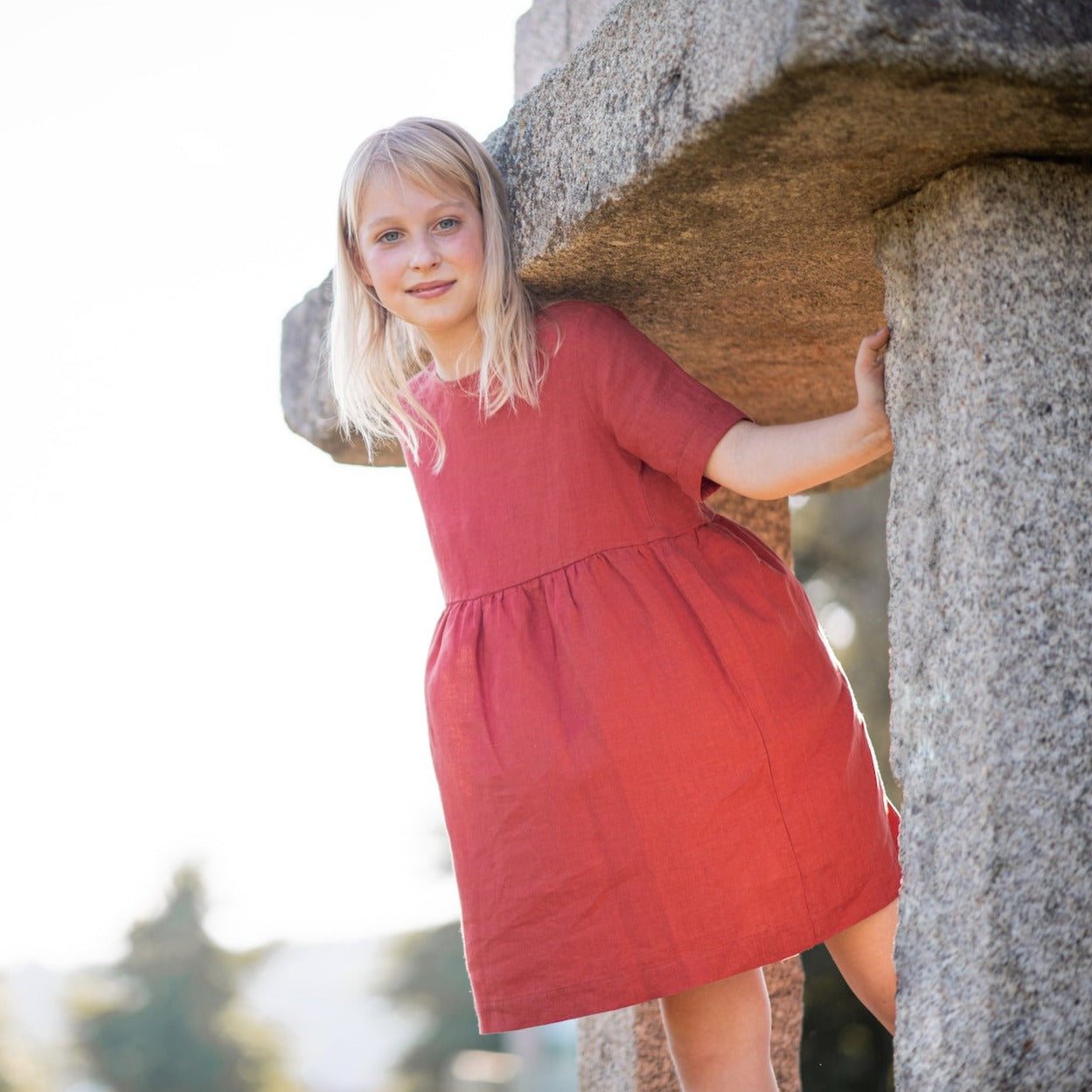 A modern casual dress in terracotta color made of soft, breathable linen with rolled cuffs and an olive wood button closure.