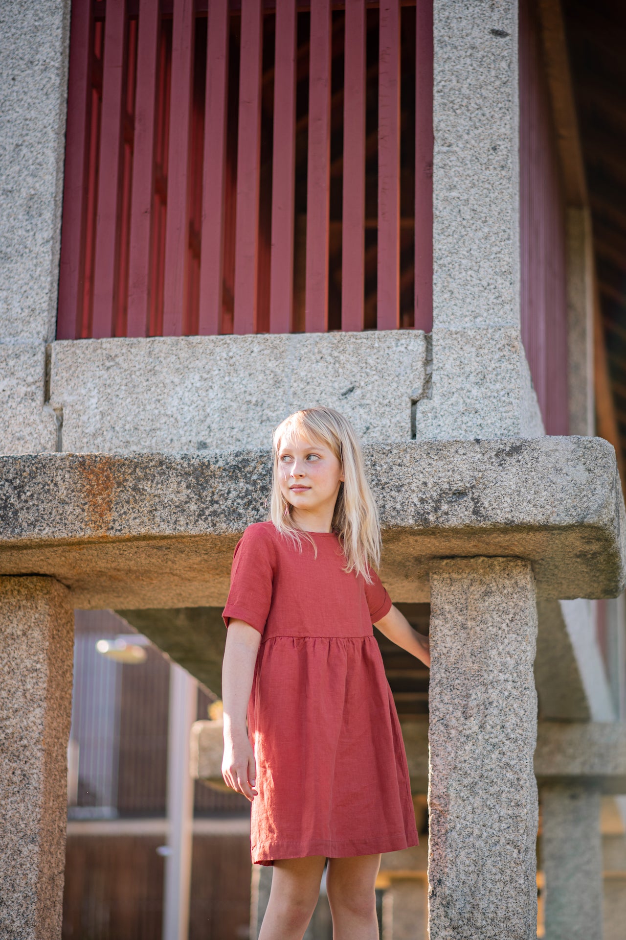 A modern casual dress in terracotta color made of soft, breathable linen with rolled cuffs and an olive wood button closure.