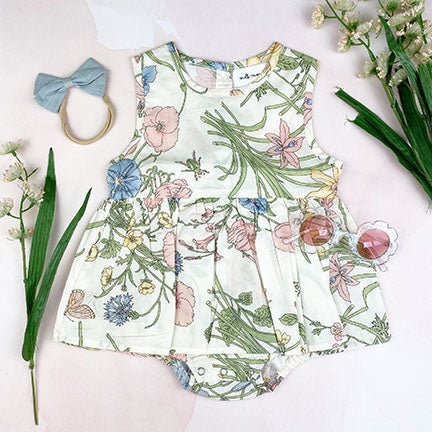 A charming ellerie onesie dress featuring a white base with a colorful spring fleur print, designed for toddlers with a circle skirt and bow detail.