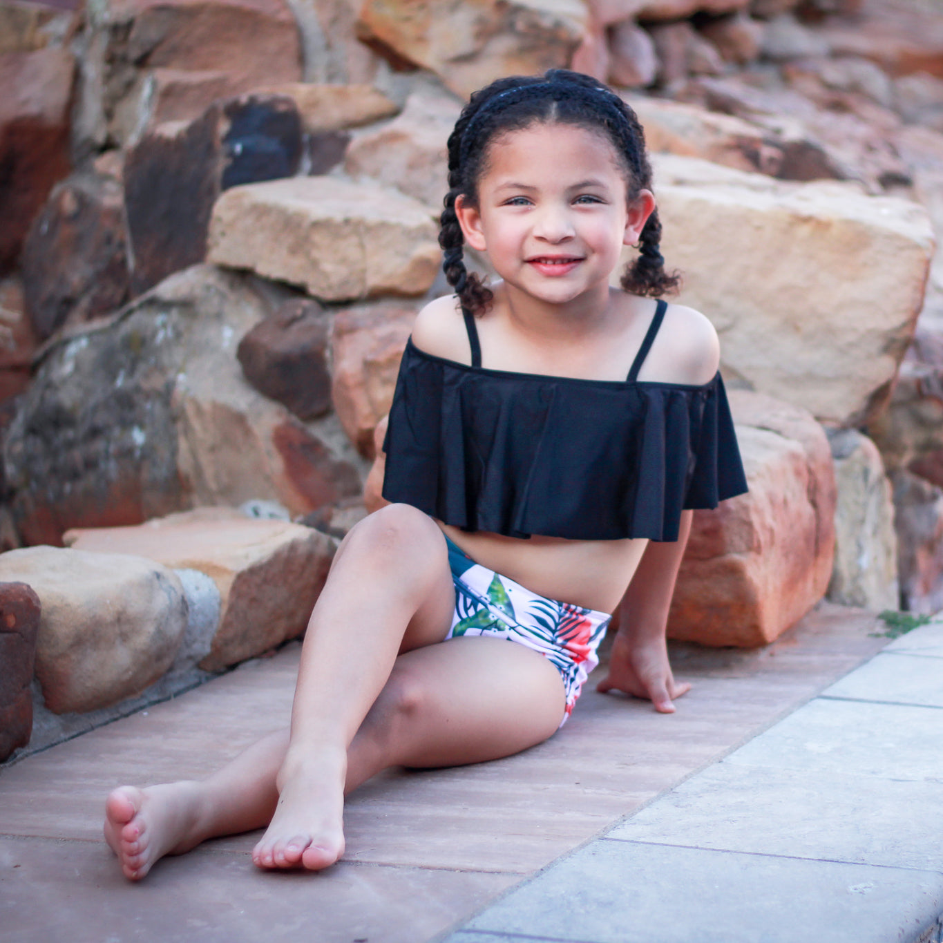 Girls 2 piece black ruffle pink tropical bikini featuring a light pink off-the-shoulder top and high-waisted tropical print bottom.