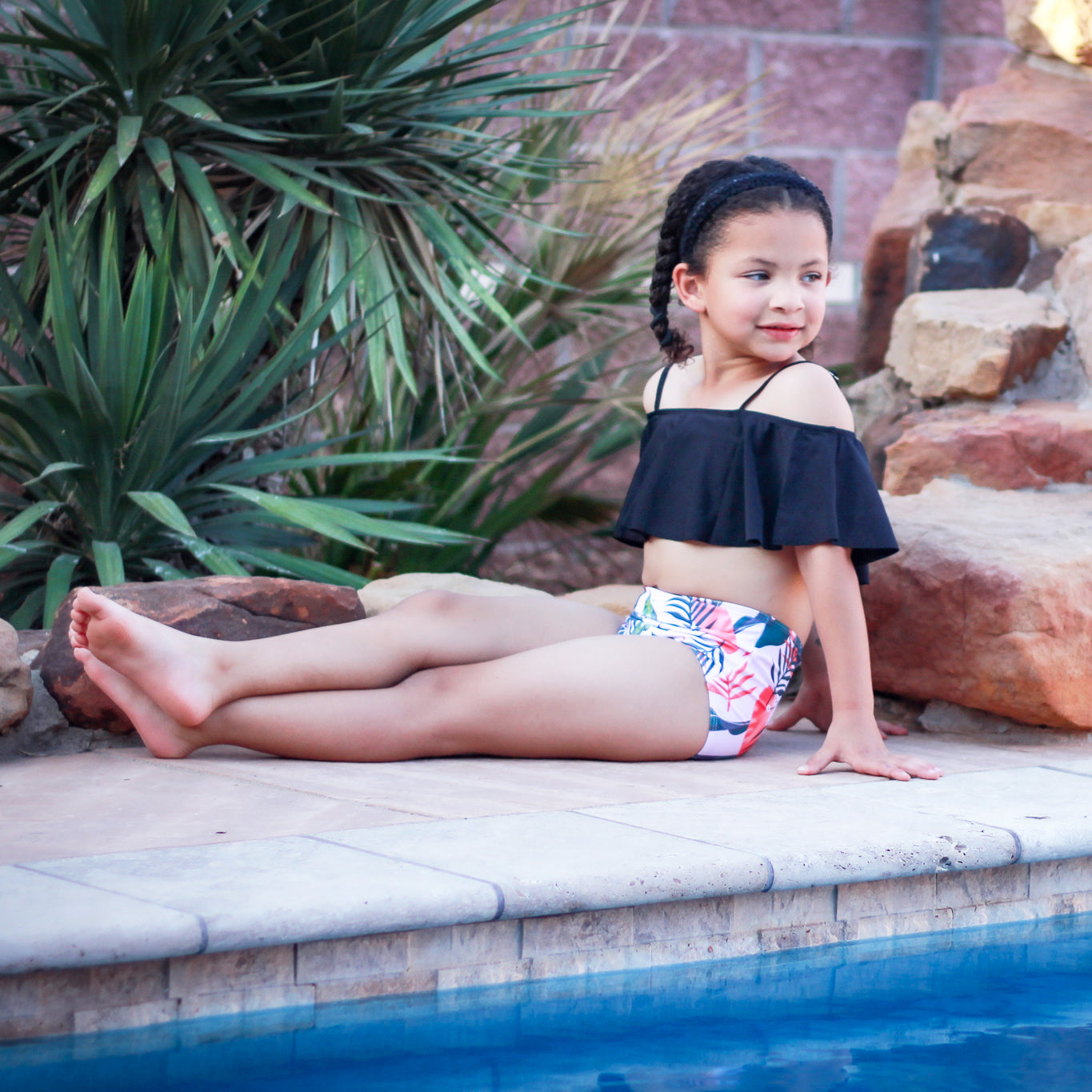 Girls 2 piece black ruffle pink tropical bikini featuring a light pink off-the-shoulder top and high-waisted tropical print bottom.