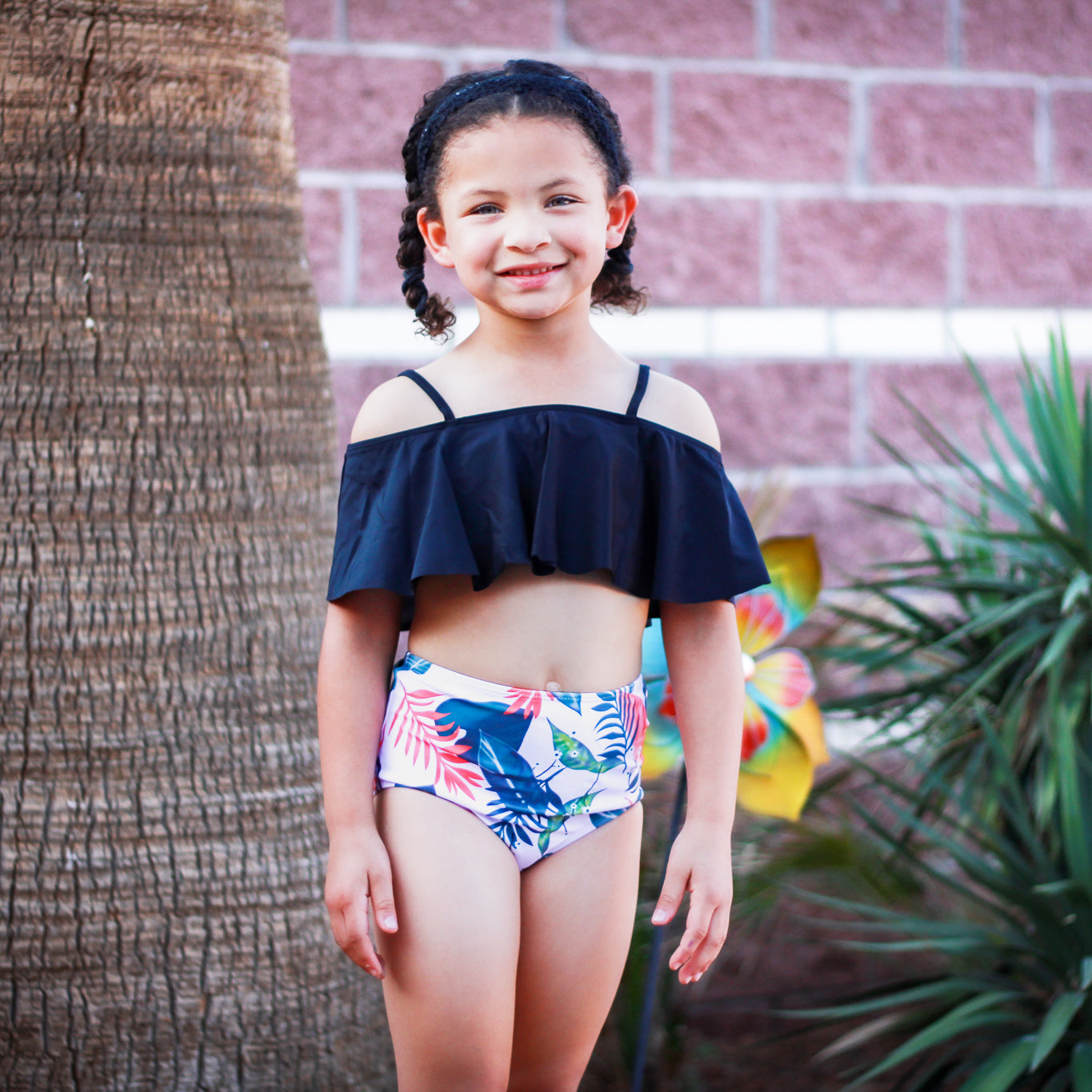 Girls 2 piece black ruffle pink tropical bikini featuring a light pink off-the-shoulder top and high-waisted tropical print bottom.