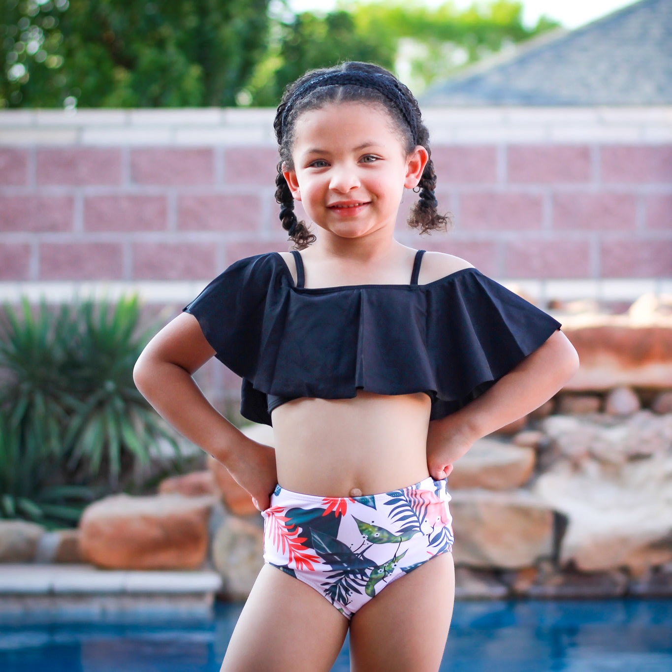 Girls 2 piece black ruffle pink tropical bikini featuring a light pink off-the-shoulder top and high-waisted tropical print bottom.