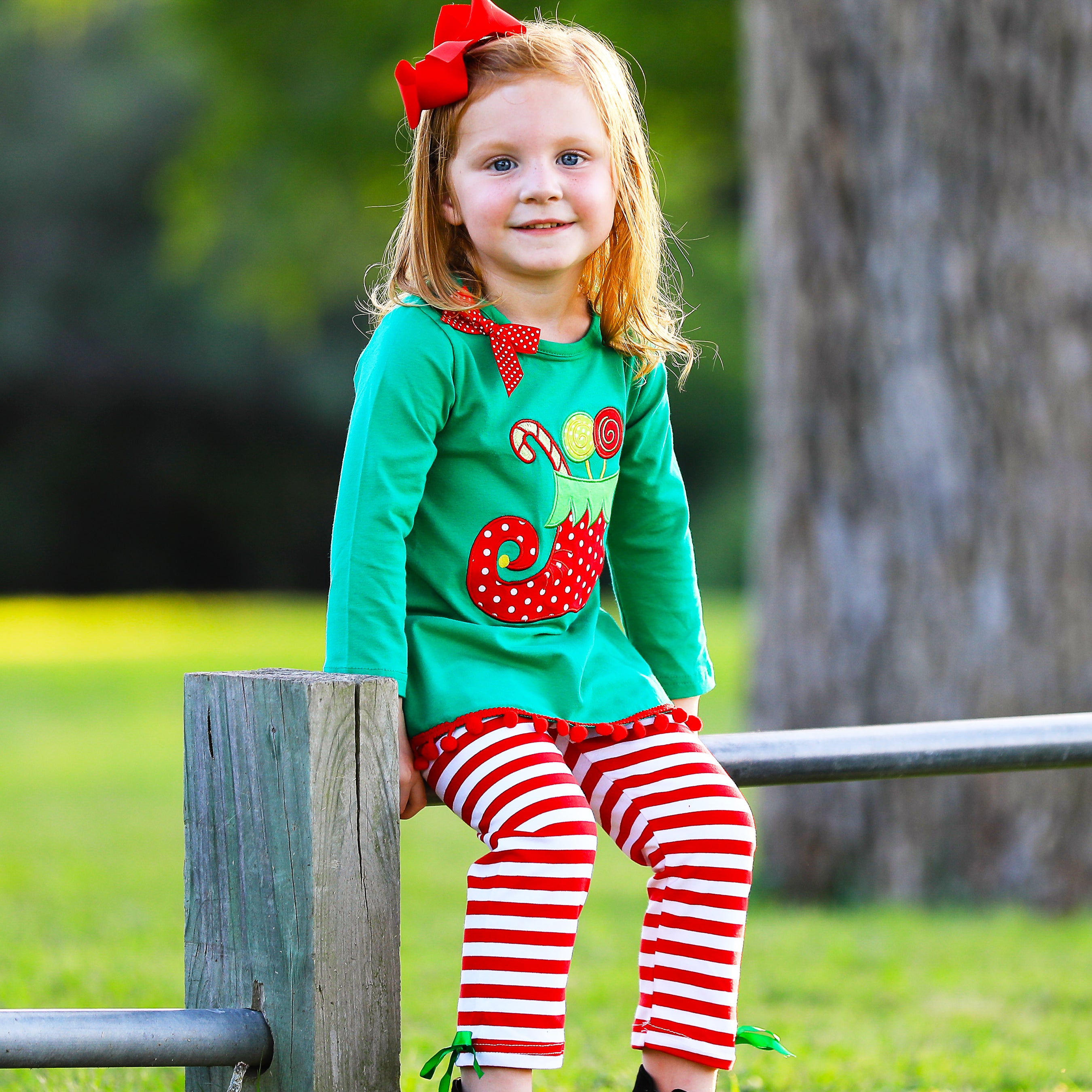 A festive girls outfit featuring an Elf Stocking top with pom pom trim and red & white striped pants, perfect for Christmas celebrations.