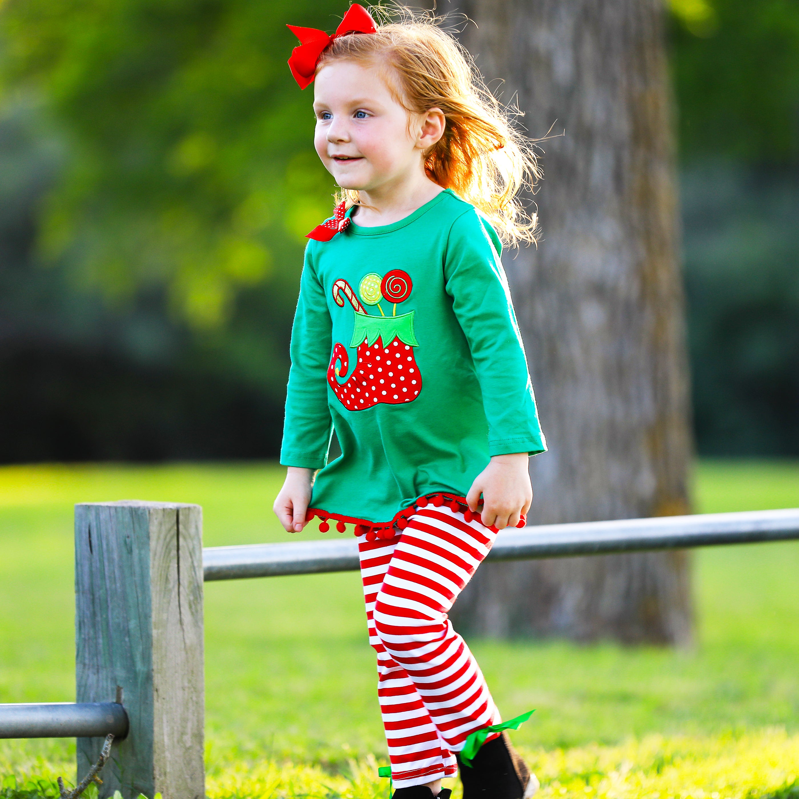 A festive girls outfit featuring an Elf Stocking top with pom pom trim and red & white striped pants, perfect for Christmas celebrations.