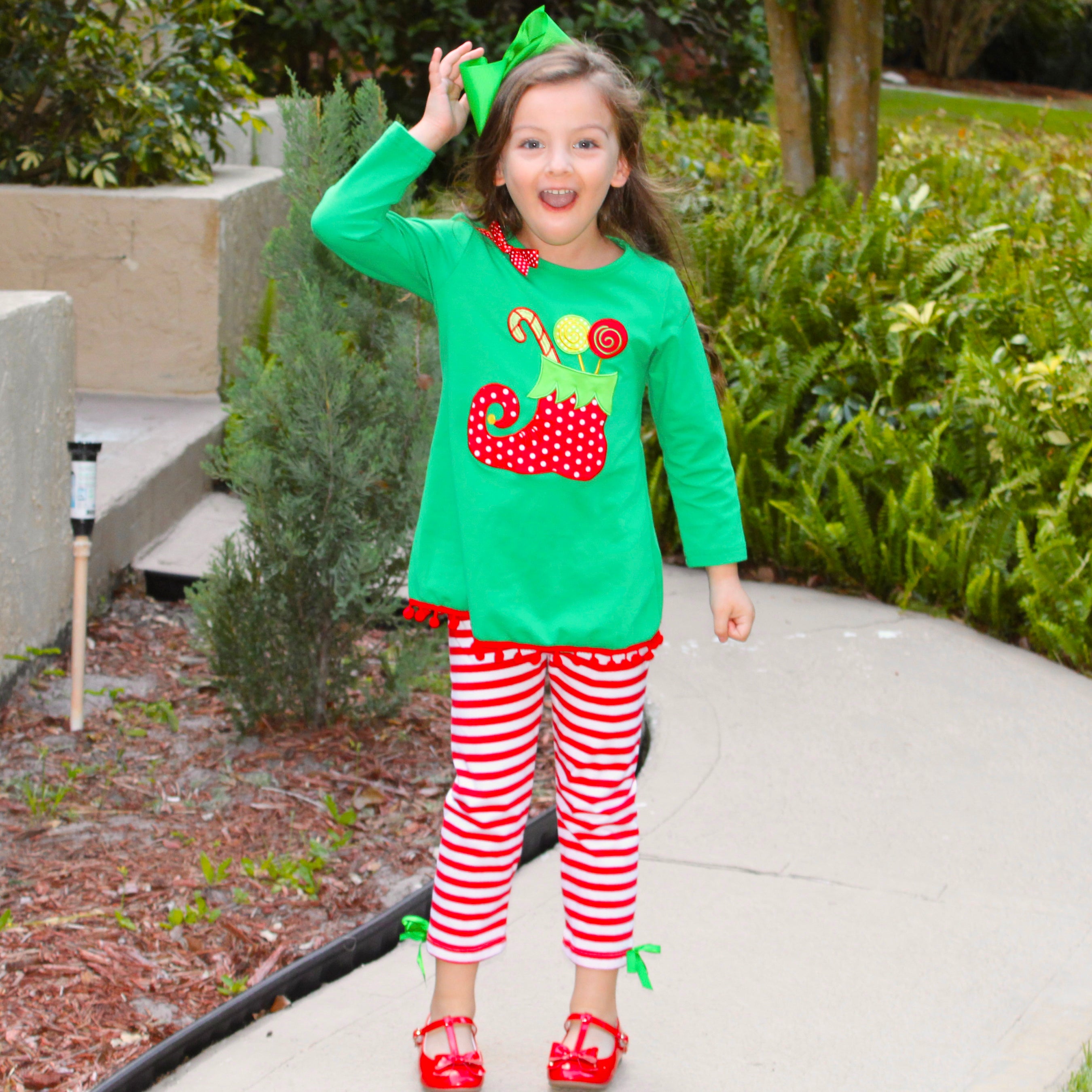 A festive girls outfit featuring an Elf Stocking top with pom pom trim and red & white striped pants, perfect for Christmas celebrations.