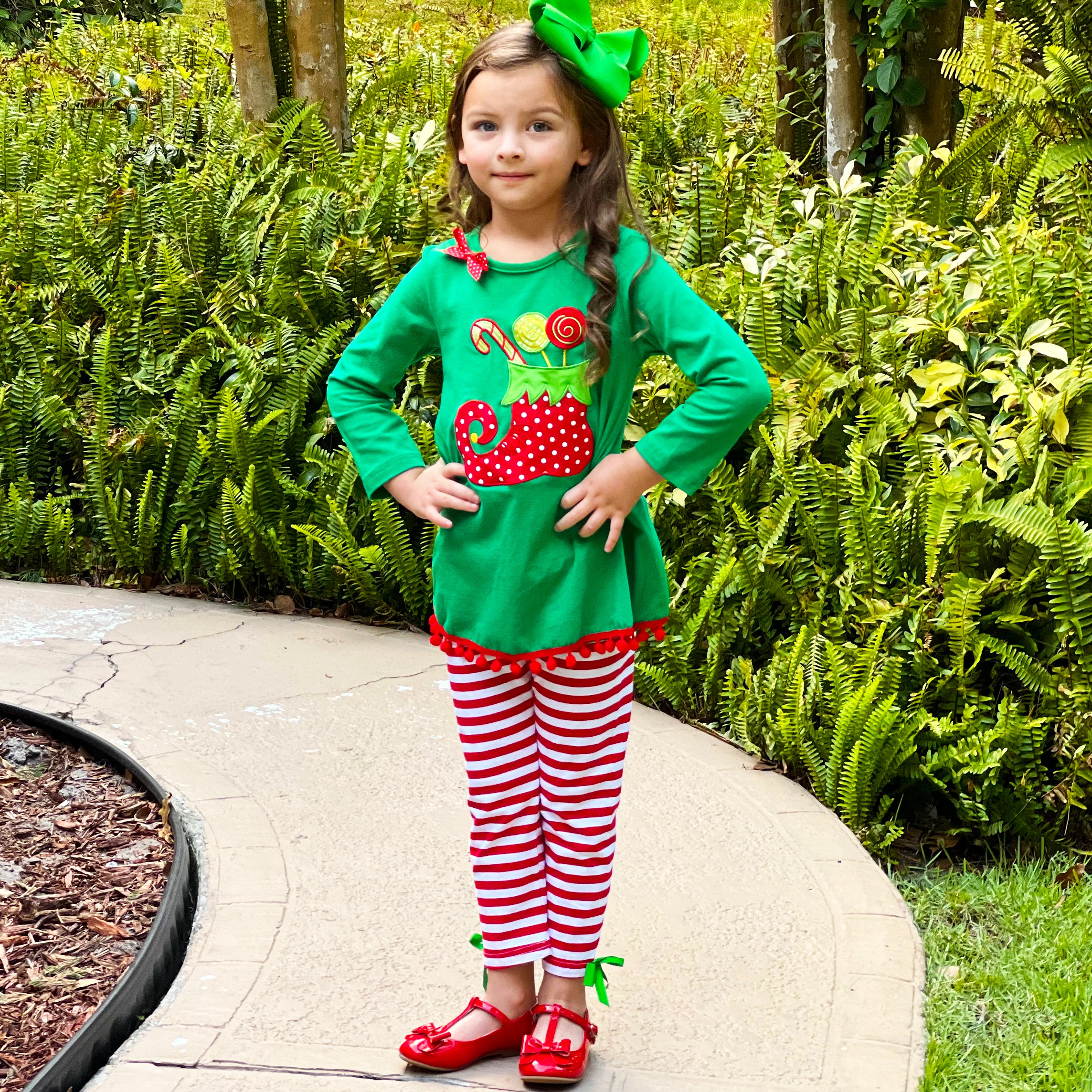 A festive girls outfit featuring an Elf Stocking top with pom pom trim and red & white striped pants, perfect for Christmas celebrations.