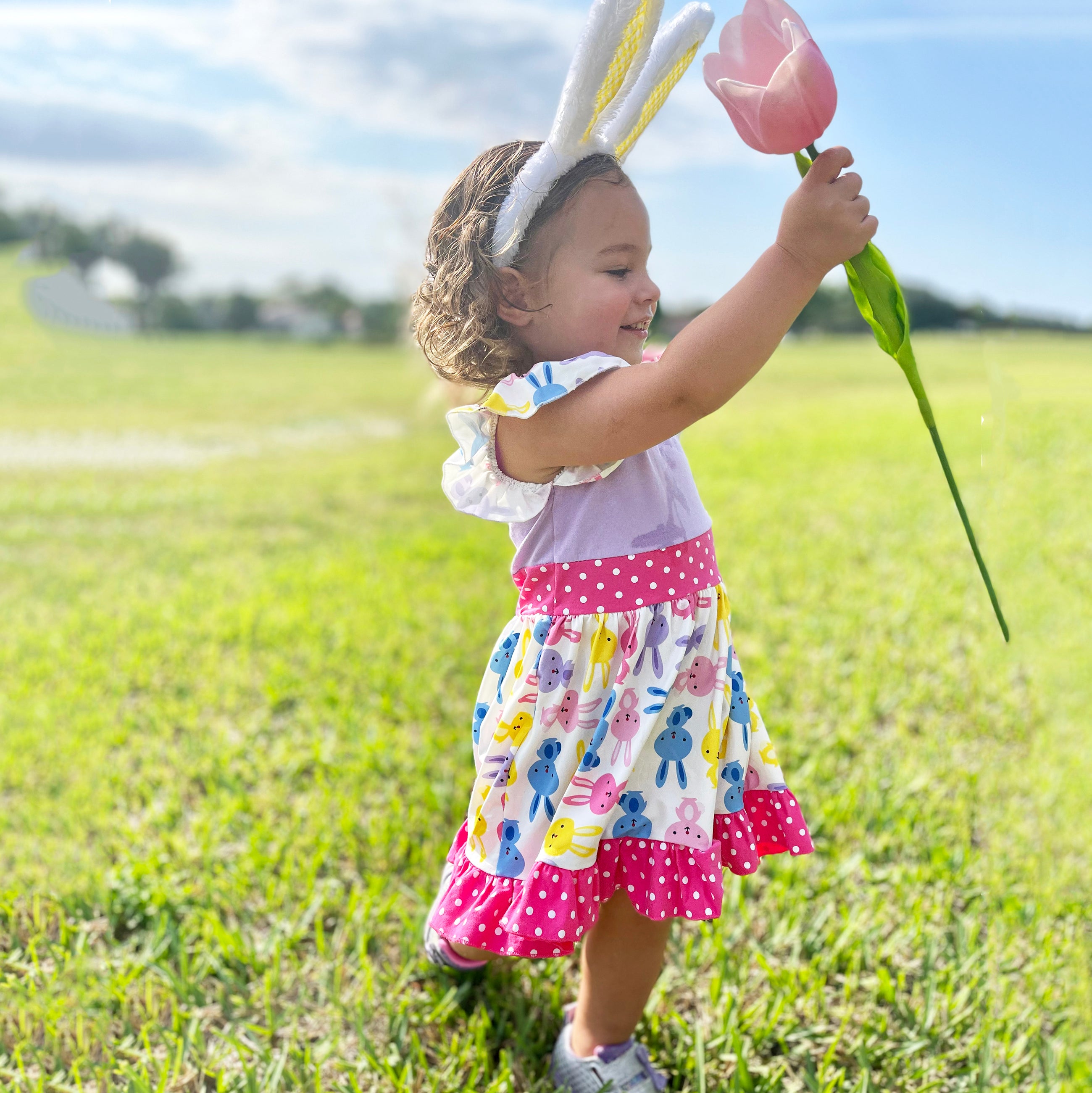 Girls Easter Bunny Dress featuring ruffles, angel cap sleeves, and a playful bunny print in pink and purple.