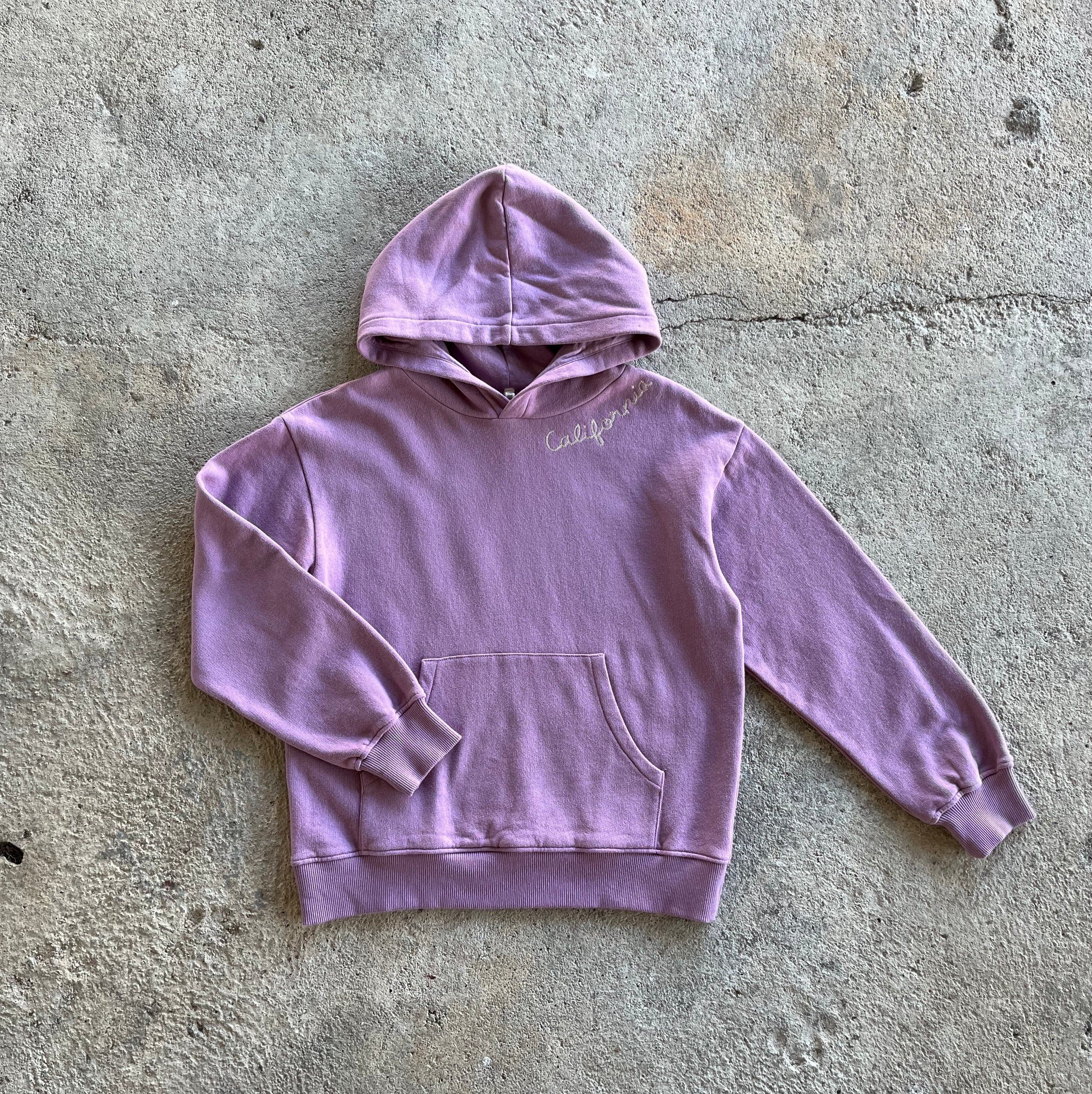 A vibrant orchid-colored kids hoodie featuring long sleeves, ribbed cuffs, and a kangaroo pocket, with 'California' embroidery on the neck.