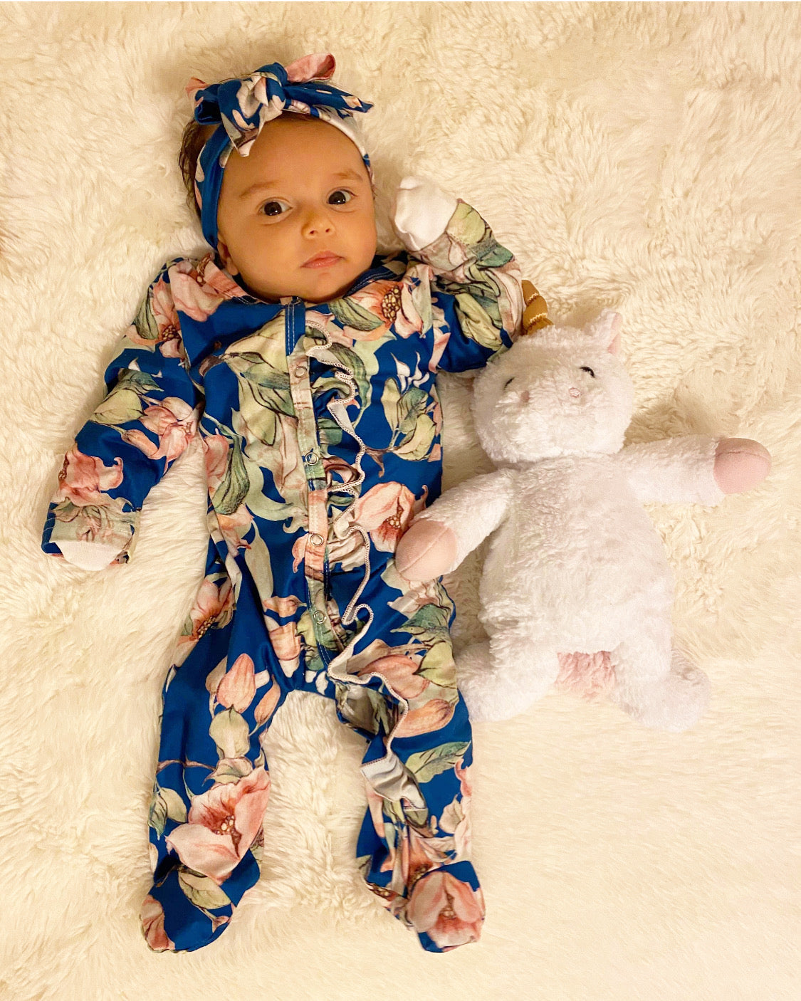 A blue floral long sleeve footed onesie with ruffle details and a matching tie headband, perfect for babies.