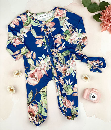 A blue floral long sleeve footed onesie with ruffle details and a matching tie headband, perfect for babies.