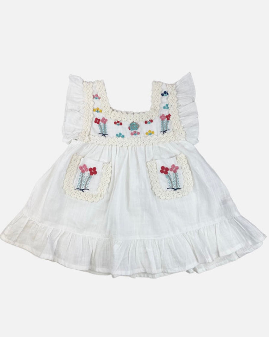 A white Maribel embroidered dress featuring colorful embroidery on the front pockets and chest, with ribbon detailing along the edges.