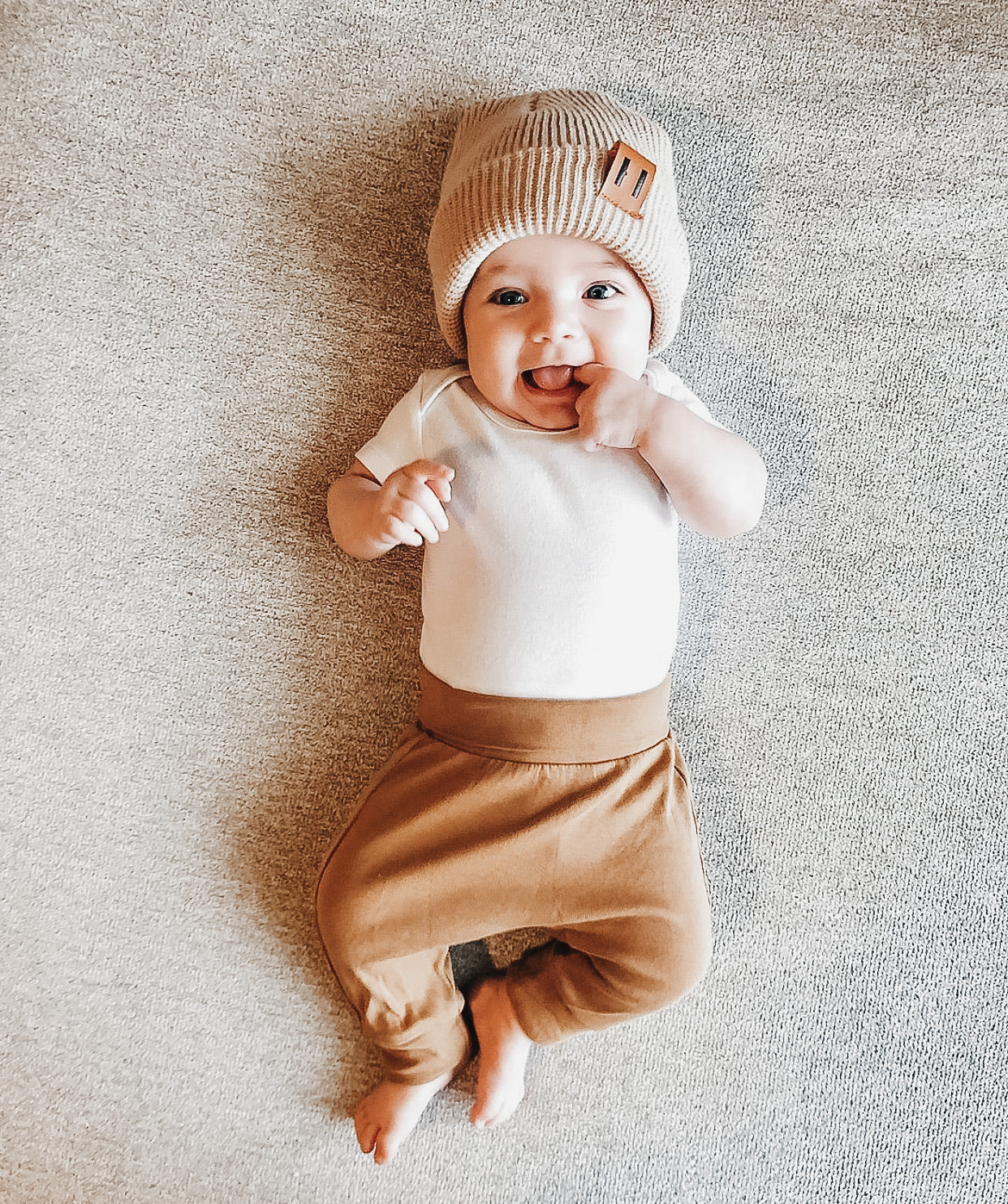 A soft and stylish neutral knit bonnet for babies, designed to fit ages 6M to 18M, featuring a secure brown tag.