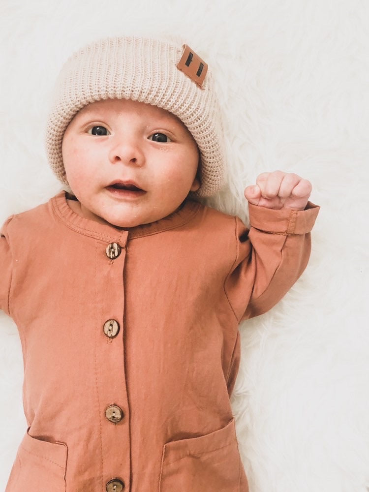 A soft and stylish neutral knit bonnet for babies, designed to fit ages 6M to 18M, featuring a secure brown tag.