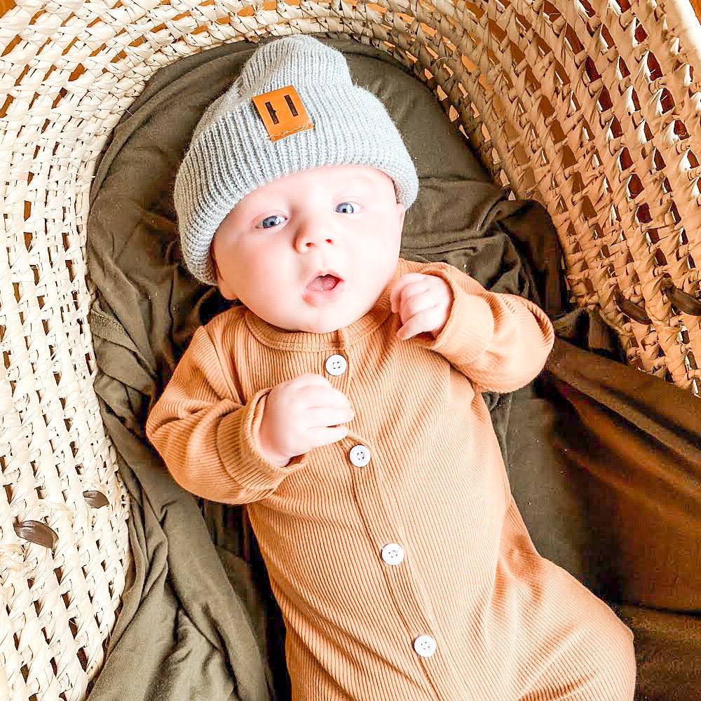 A soft and stylish neutral knit bonnet for babies, designed to fit ages 6M to 18M, featuring a secure brown tag.