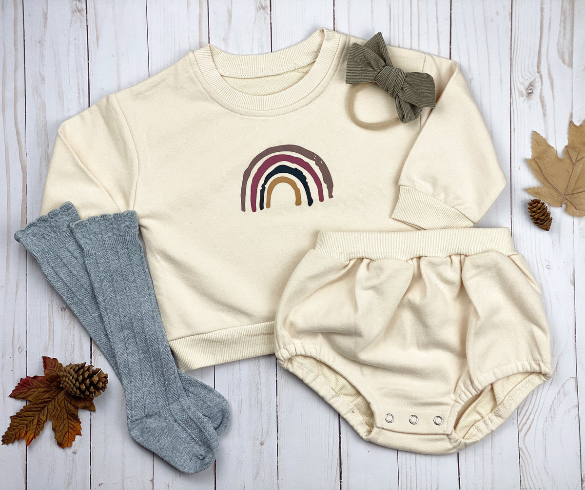 A cozy rainbow 2 pc sweatshirt set in toast color featuring a vintage rainbow design on the sweatshirt and bubble shorts with elastic waistband.