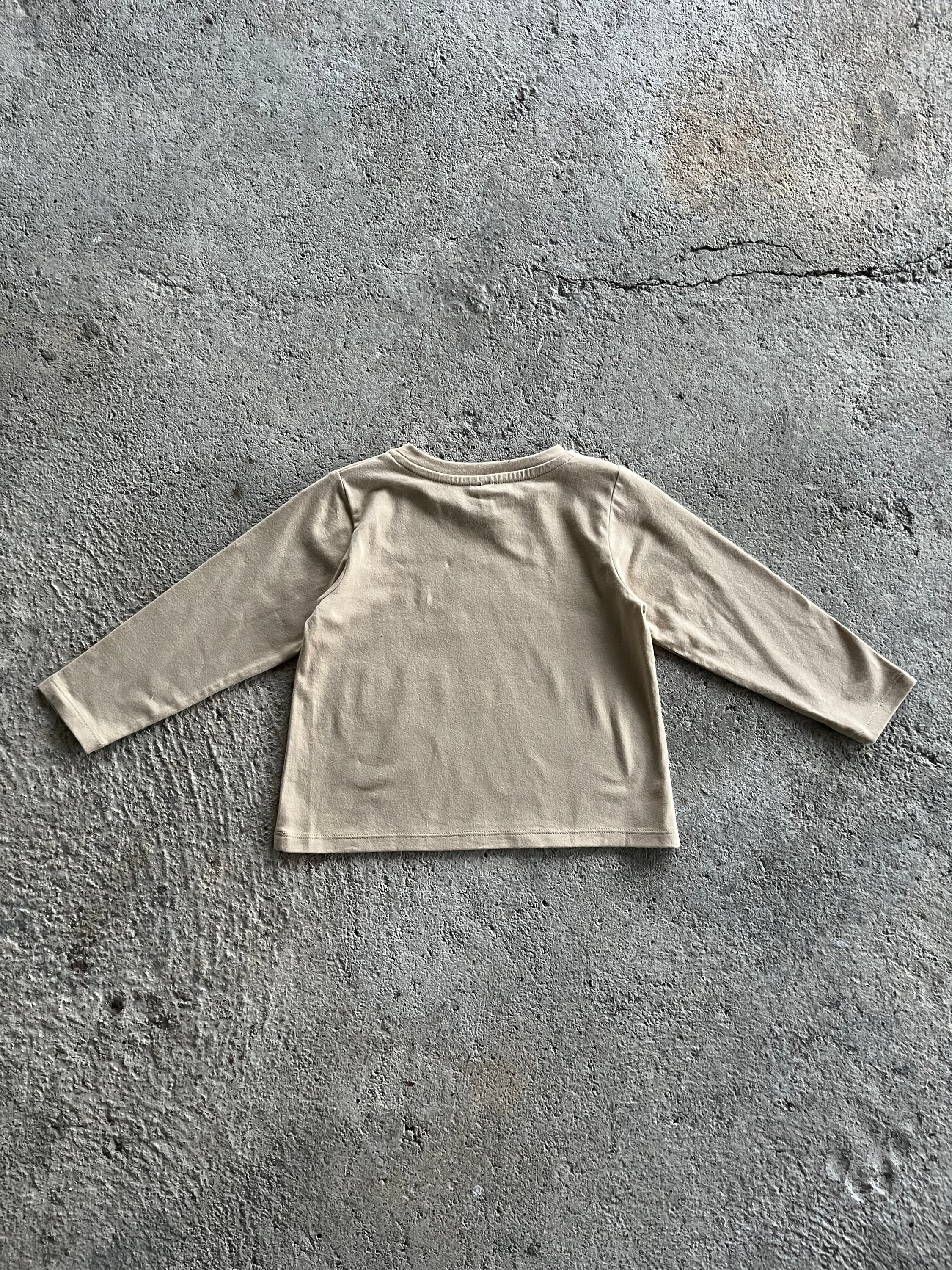 A long sleeve baby shirt in latte color featuring a chocolate rainbow print, made from 100% organic cotton.