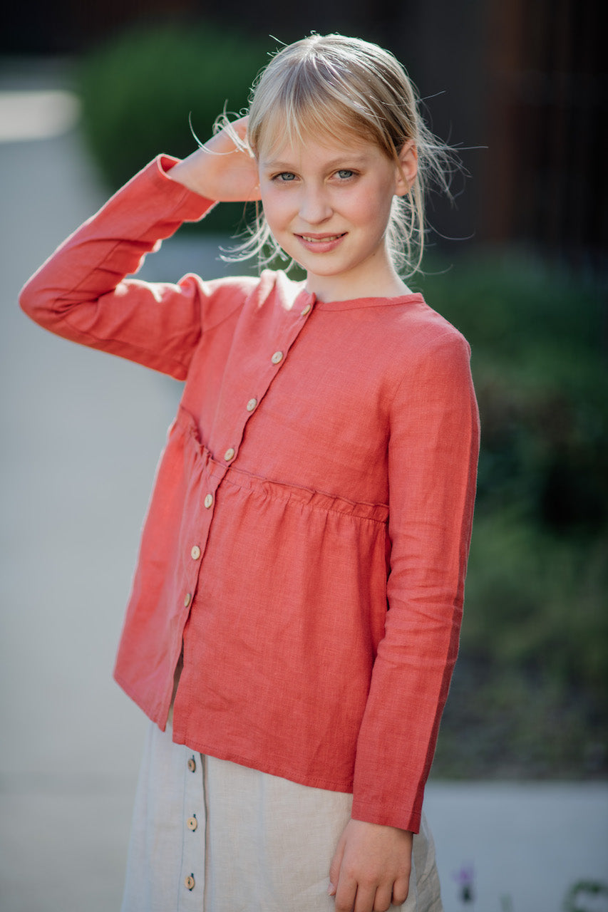 A casual long-sleeve shirt in terracotta color with olive wood buttons and a frilled elasticised waist, made from 100% breathable linen.