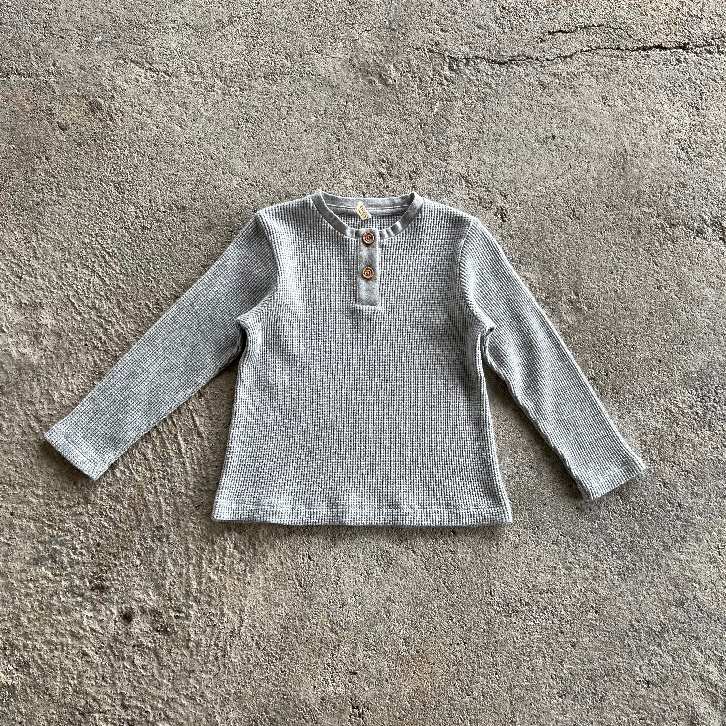 A soft, heather grey long sleeve shirt for babies and toddlers with a round collar and wood buttons, made from 100% organic cotton.