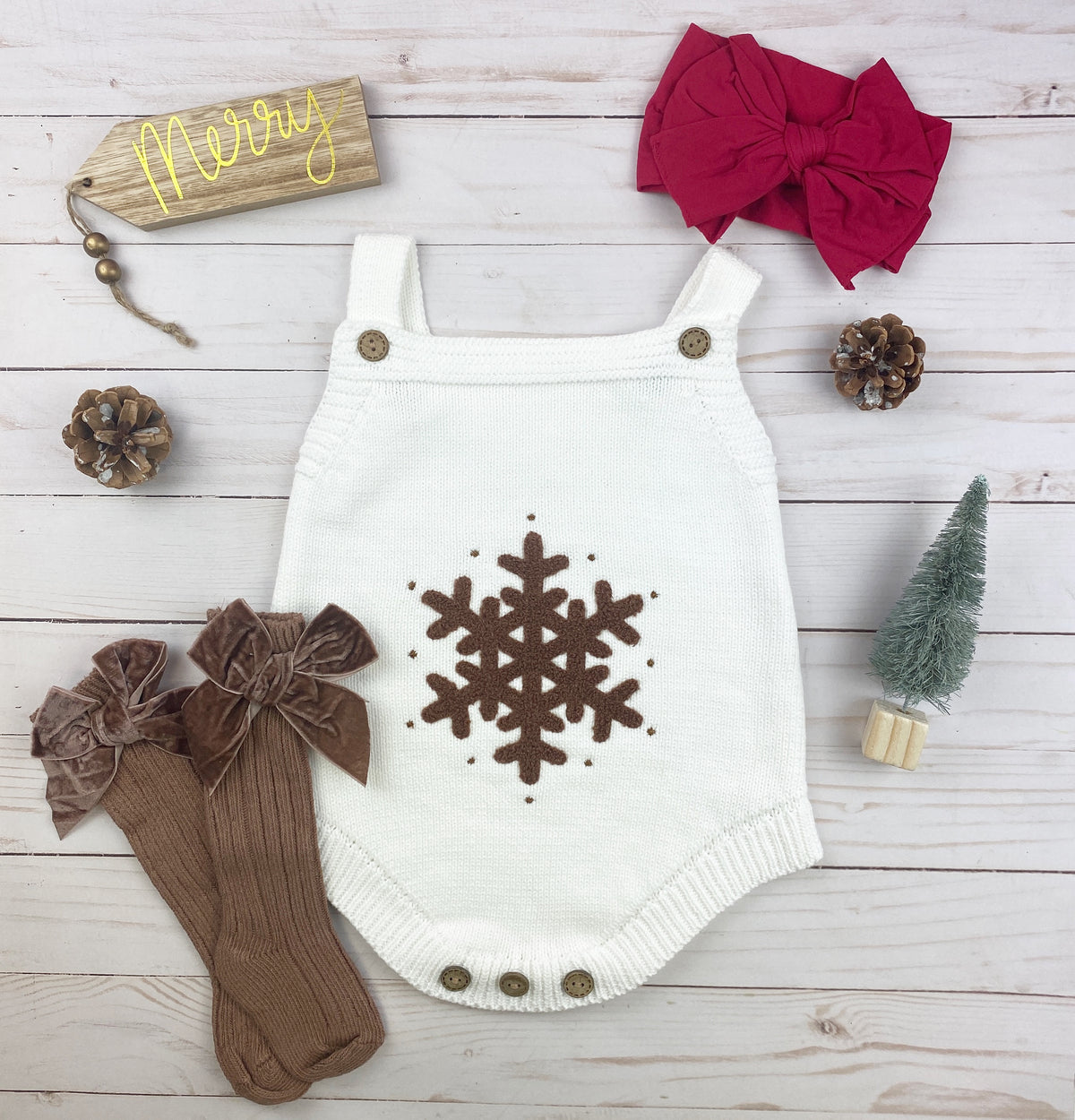 A cozy white knitted onesie for babies featuring a brown crochet snowflake design and wooden button details, perfect for holiday wear.