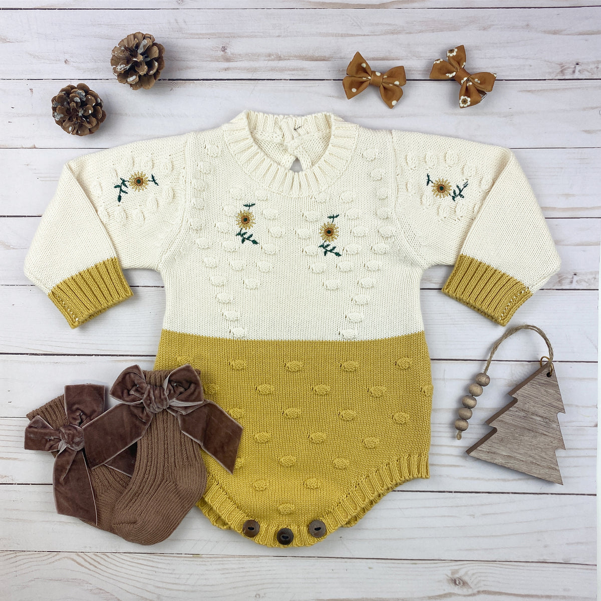 A cozy sunflower knitted onesie in gold and cream, featuring crochet sunflower details and wooden buttons for easy diaper changes.