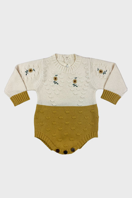 A cozy sunflower knitted onesie in gold and cream, featuring crochet sunflower details and wooden buttons for easy diaper changes.