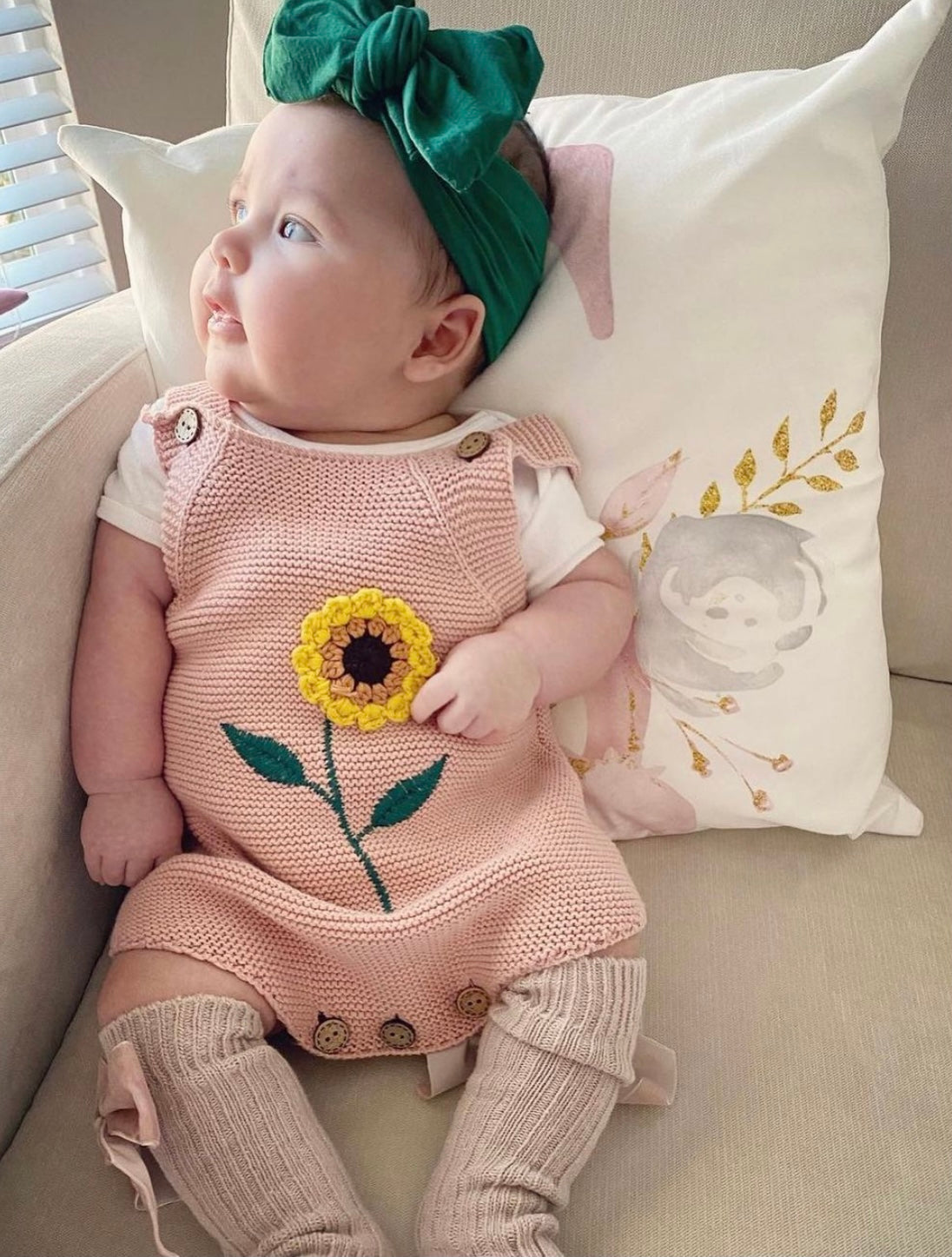 A beautiful rose and white knitted onesie featuring sunflower crochet detail and wooden button closures, perfect for babies.