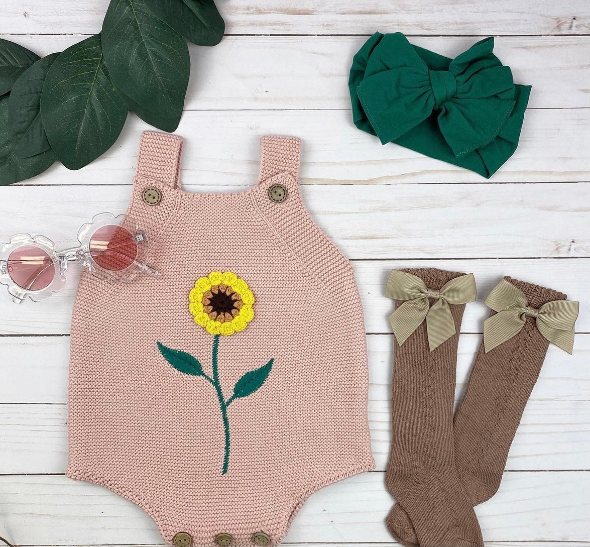 A beautiful rose and white knitted onesie featuring sunflower crochet detail and wooden button closures, perfect for babies.