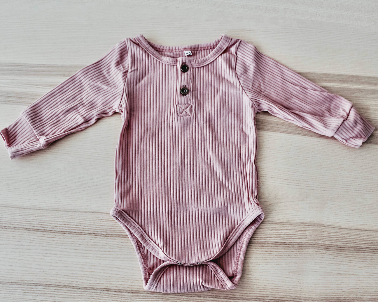 A soft ribbed bodysuit for babies, made from cotton and spandex, showcasing its stylish design and available sizes.