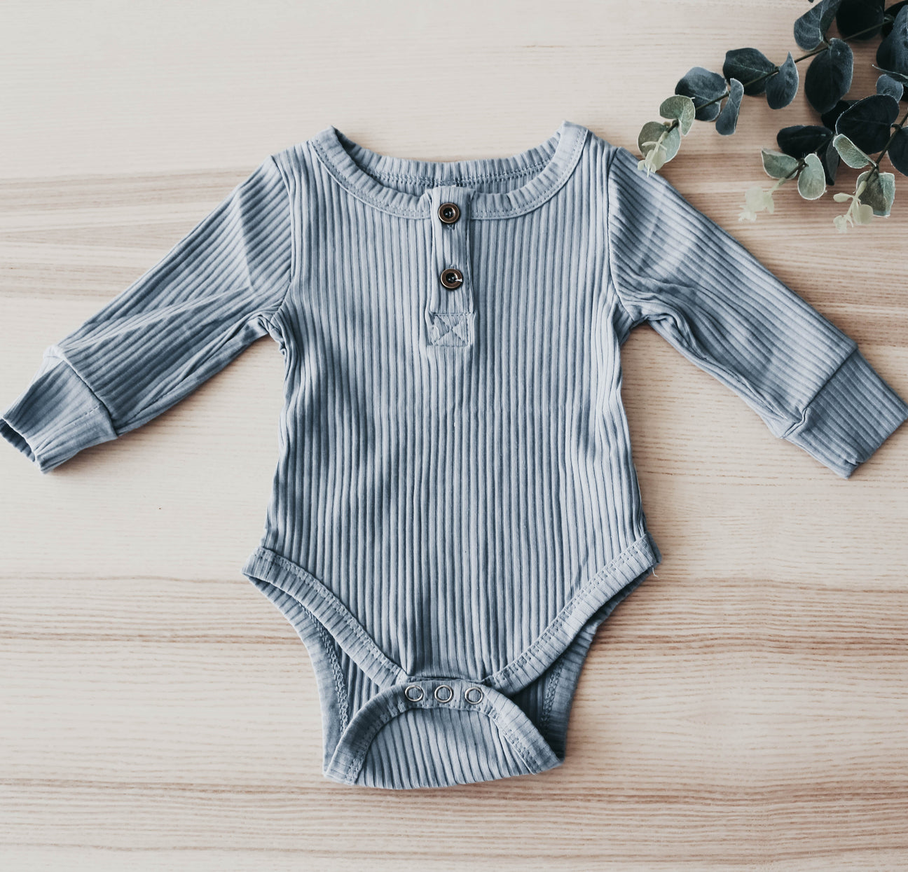 A soft ribbed bodysuit for babies, made from cotton and spandex, showcasing its stylish design and available sizes.