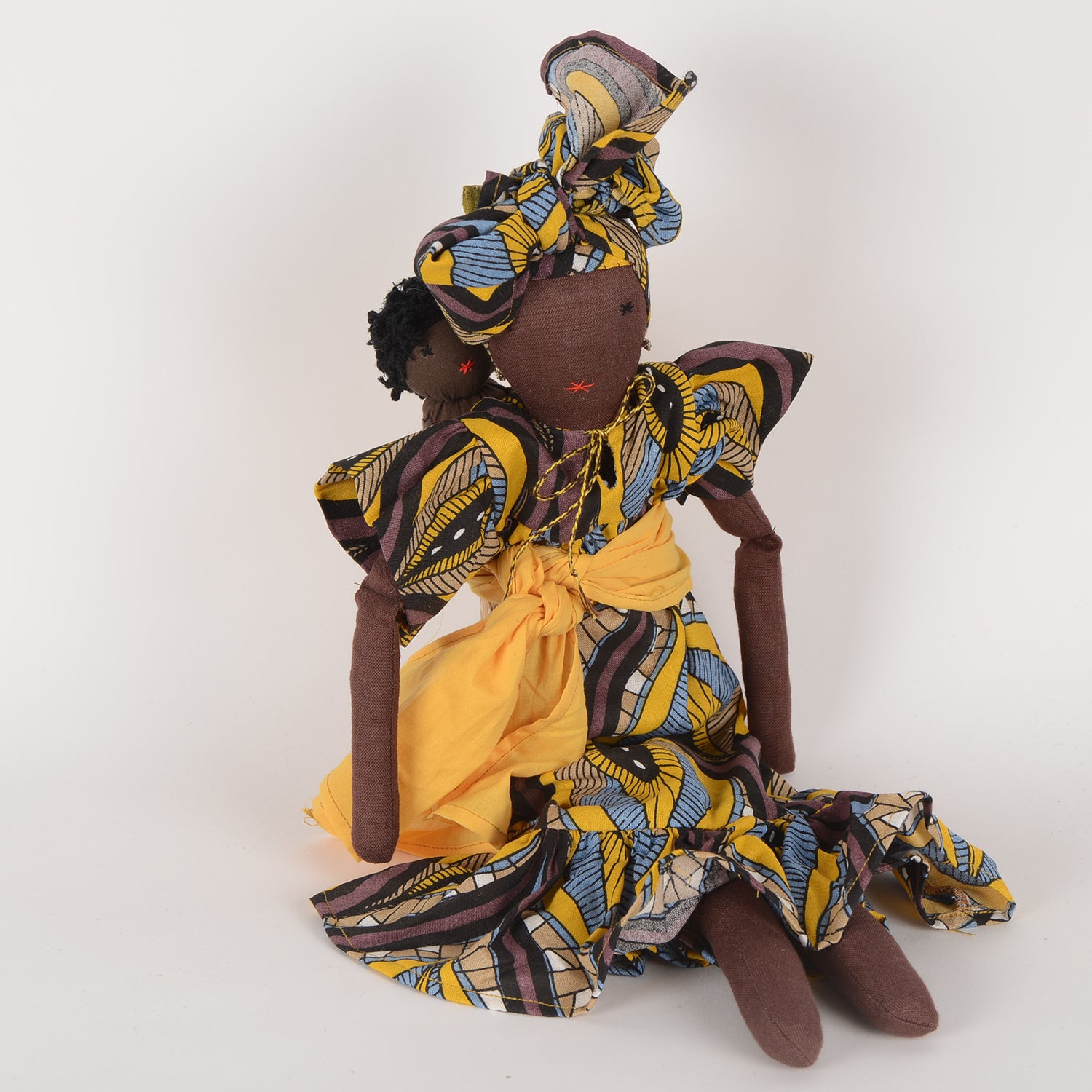 Imani doll with vibrant African print kaftan and regal turban, holding a baby, symbolizing maternal strength and cultural diversity.