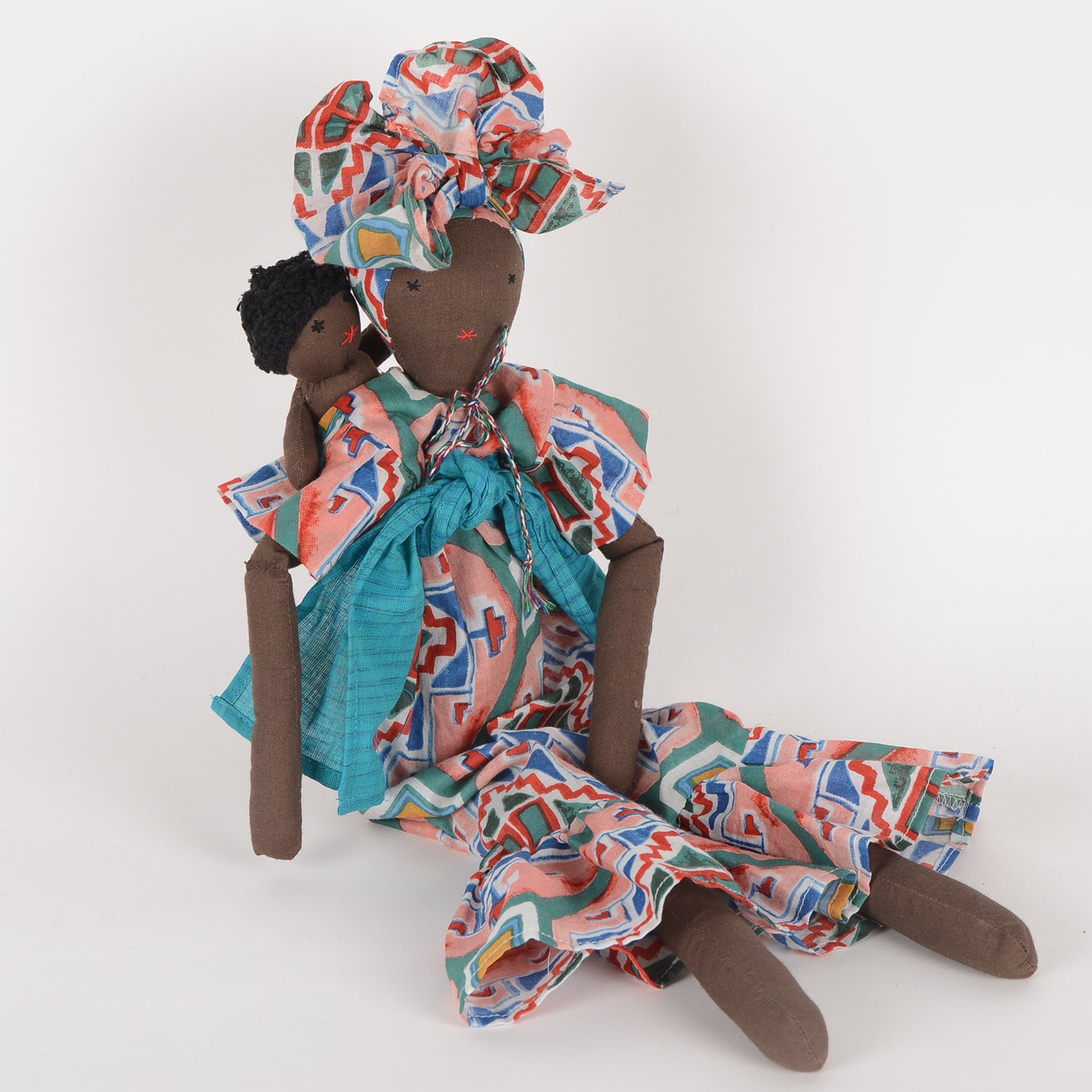 Imani doll with vibrant African print kaftan and regal turban, holding a baby, symbolizing maternal strength and cultural diversity.