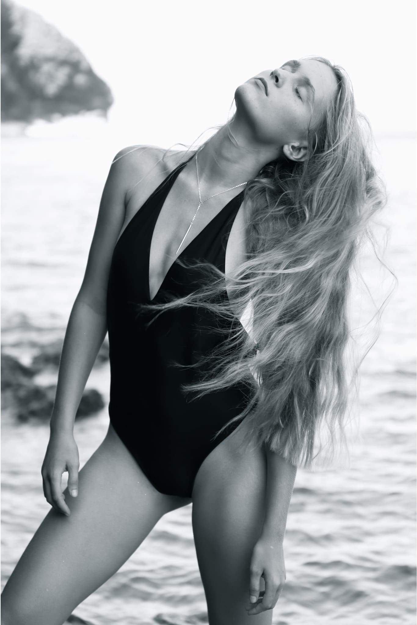 The CAROLINE PIECE in Ink Black, a stylish backless Brazilian one piece swimsuit with a plunging neckline and high cut legs, displayed elegantly.