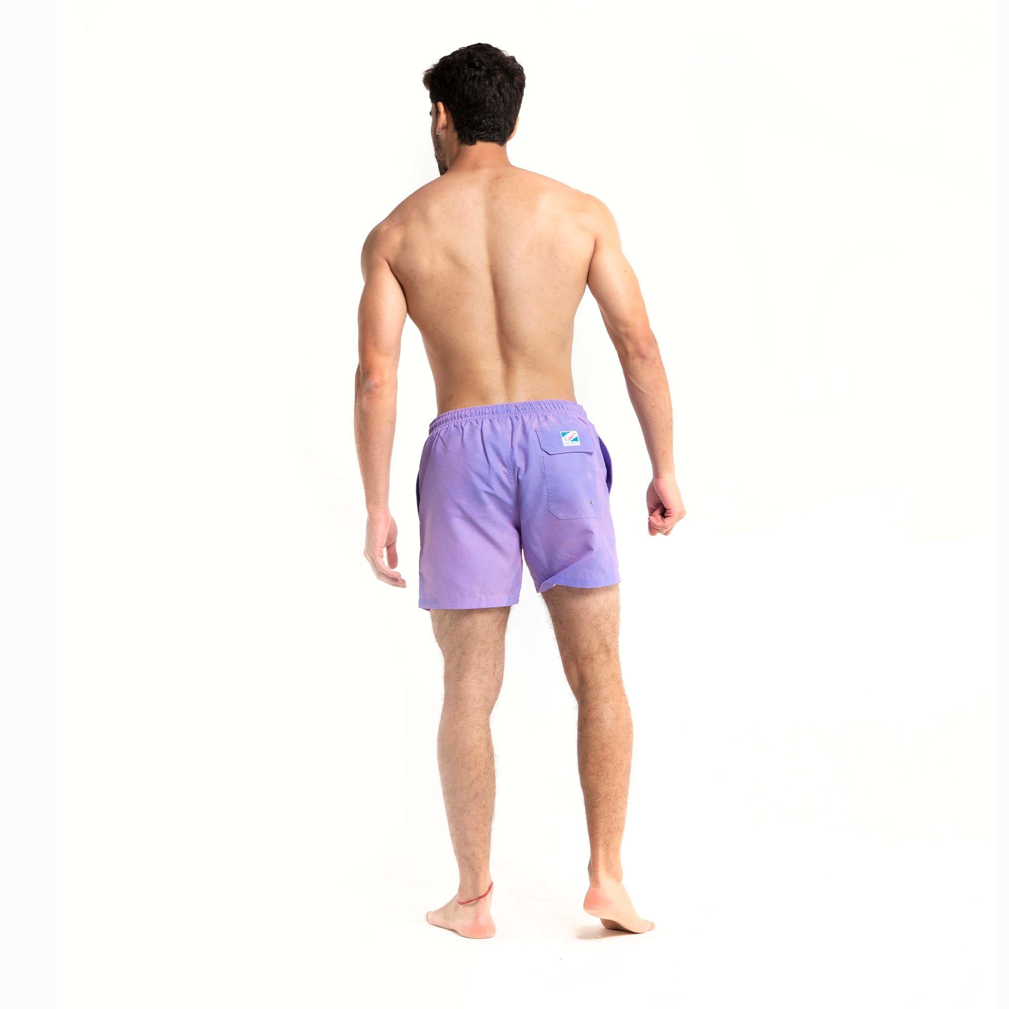 Color-changing Pink to Purple 5" Swim Trunks displayed on a beach setting, showcasing their vibrant colors and eco-friendly design.