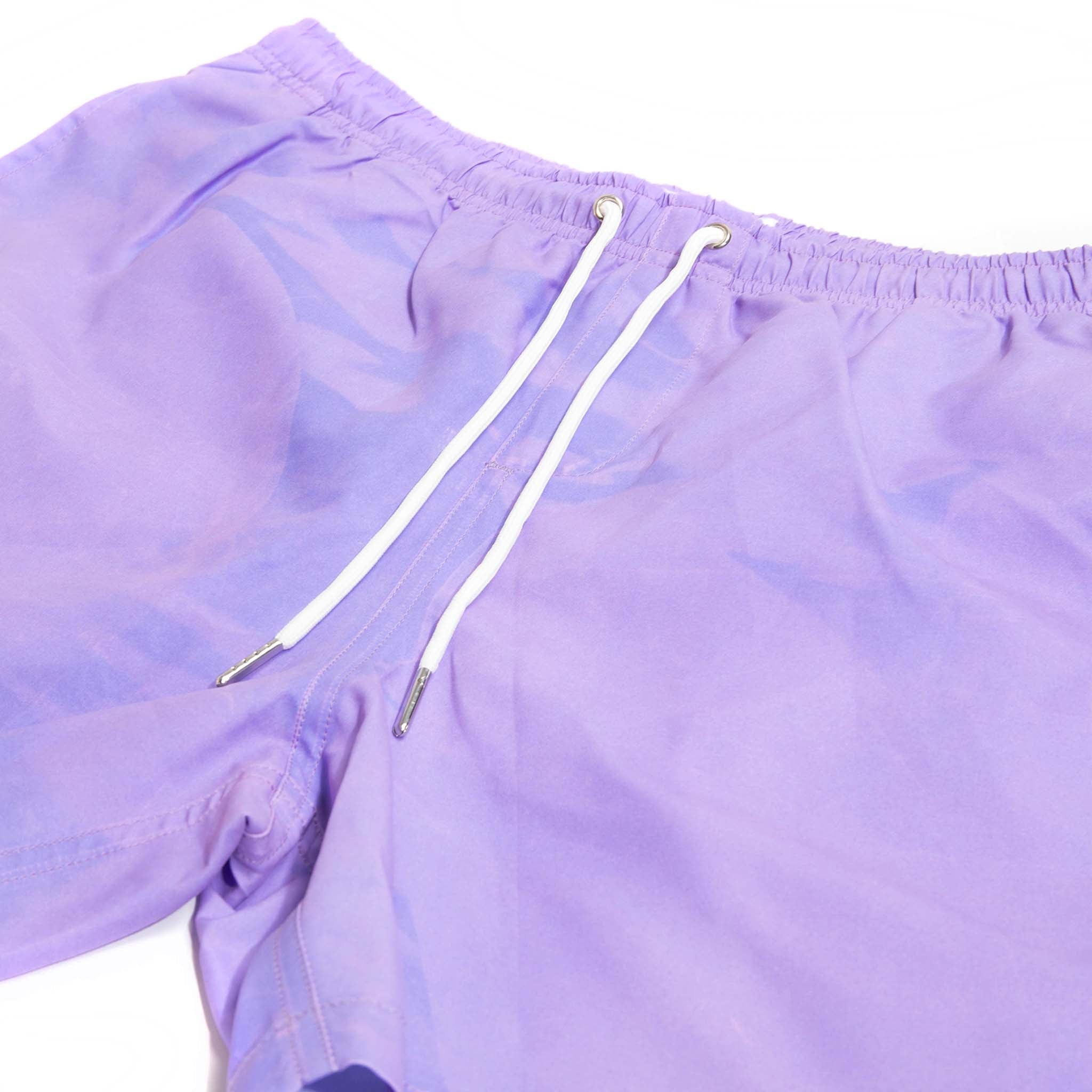 Color-changing Pink to Purple 5" Swim Trunks displayed on a beach setting, showcasing their vibrant colors and eco-friendly design.