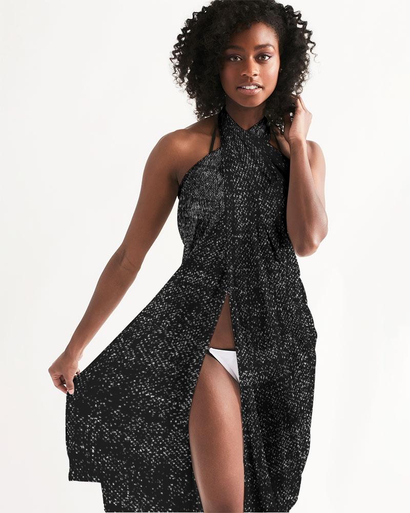 A lightweight sheer sarong swimsuit cover-up wrap in distressed black, elegantly draped over a beach chair, showcasing its flowy fabric and self-tie closure.