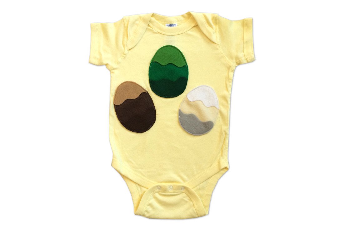 A handmade infant bodysuit featuring a unique design of three colorful dragon eggs appliquéd on the front, perfect for stylish babies.