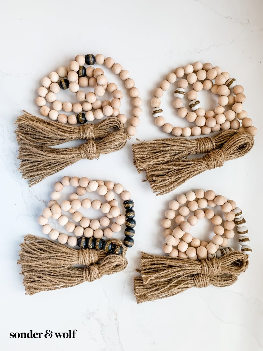 A 4ft handmade wood bead garland featuring light unfinished wood beads and four distinctive Black Kente Krobo beads, adorned with jute tassels.