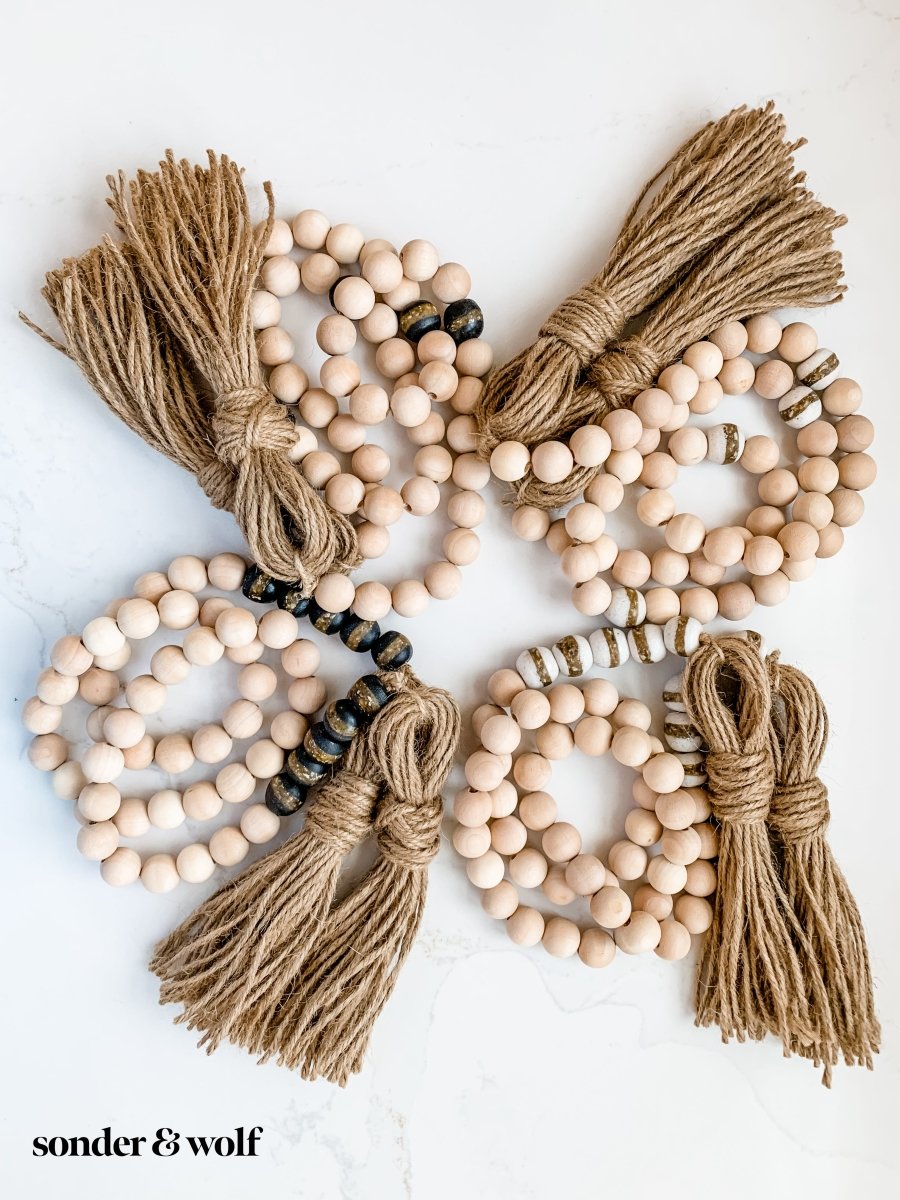 A 4ft handmade wood bead garland featuring light unfinished wood beads and four distinctive Black Kente Krobo beads, adorned with jute tassels.