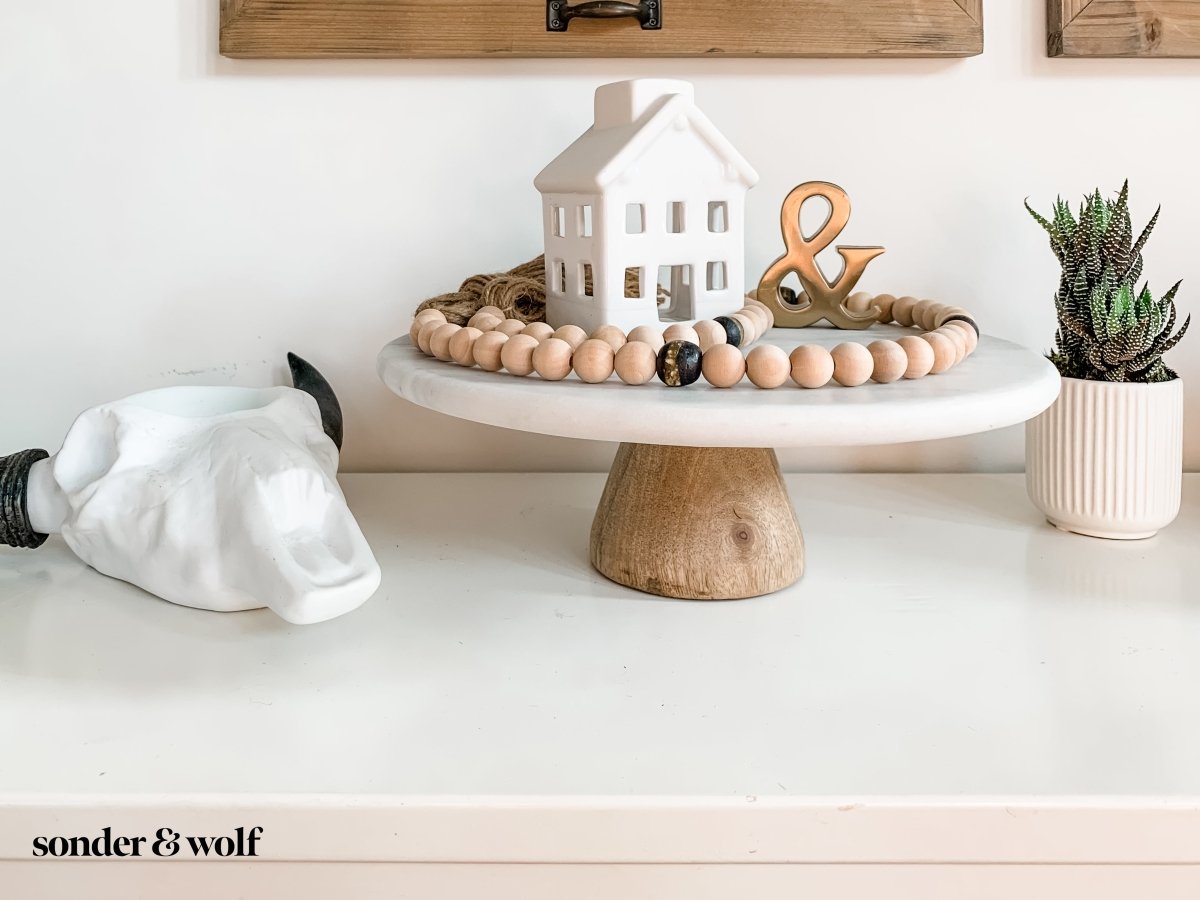 A 4ft handmade wood bead garland featuring light unfinished wood beads and four distinctive Black Kente Krobo beads, adorned with jute tassels.