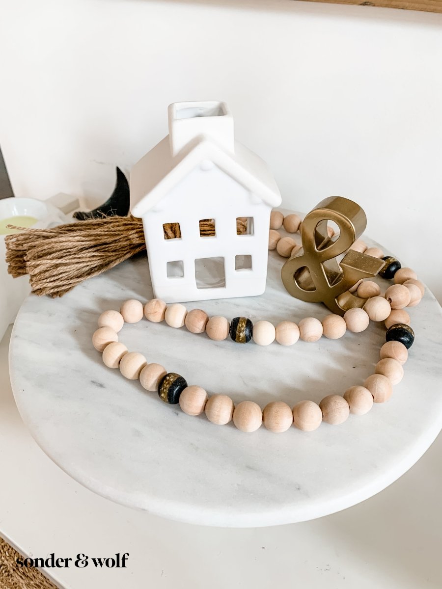 A 4ft handmade wood bead garland featuring light unfinished wood beads and four distinctive Black Kente Krobo beads, adorned with jute tassels.