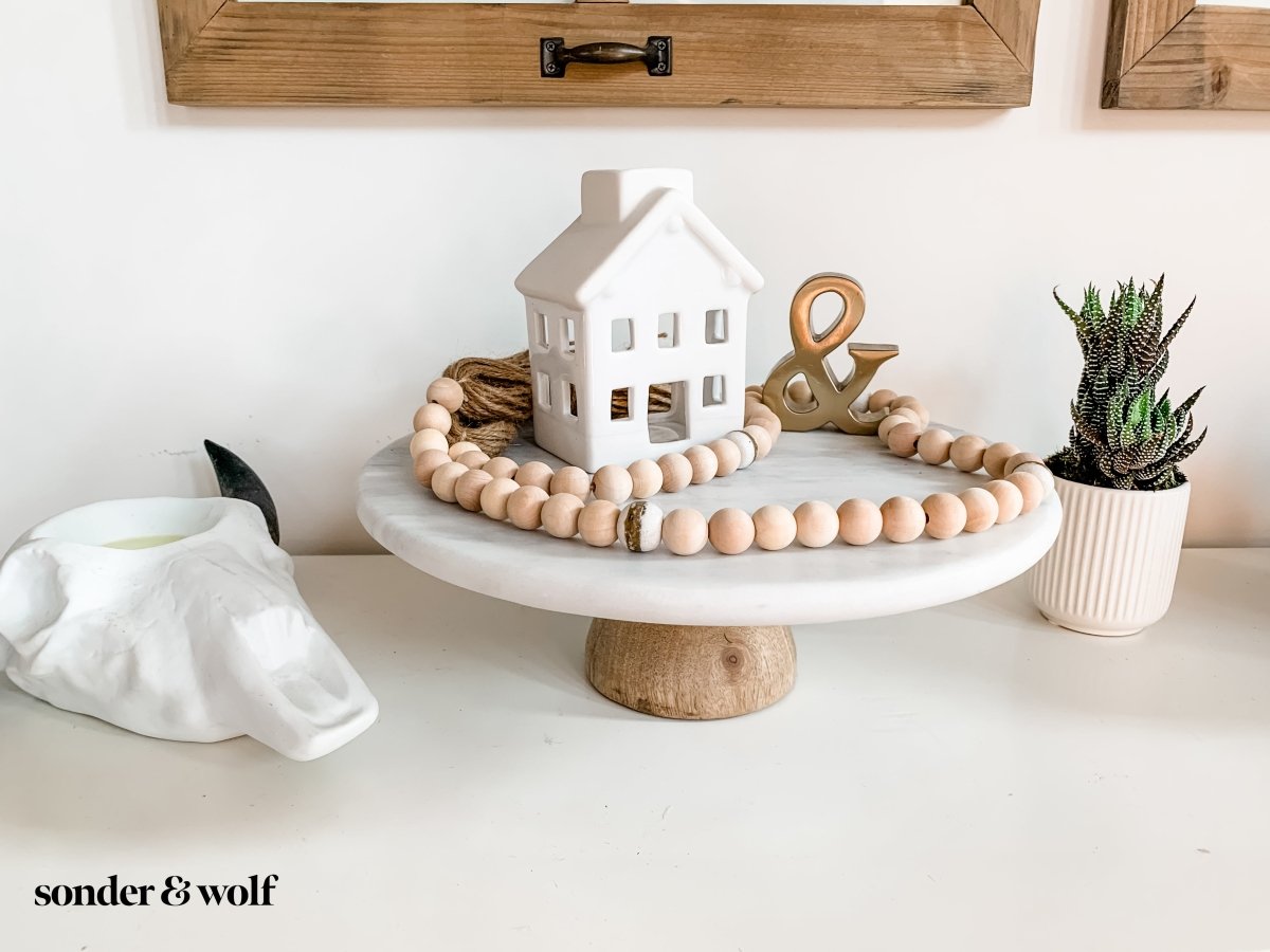 A 4ft handmade wood bead garland featuring light unfinished wood beads and four distinctive White Kente Krobo beads, adorned with jute tassels.