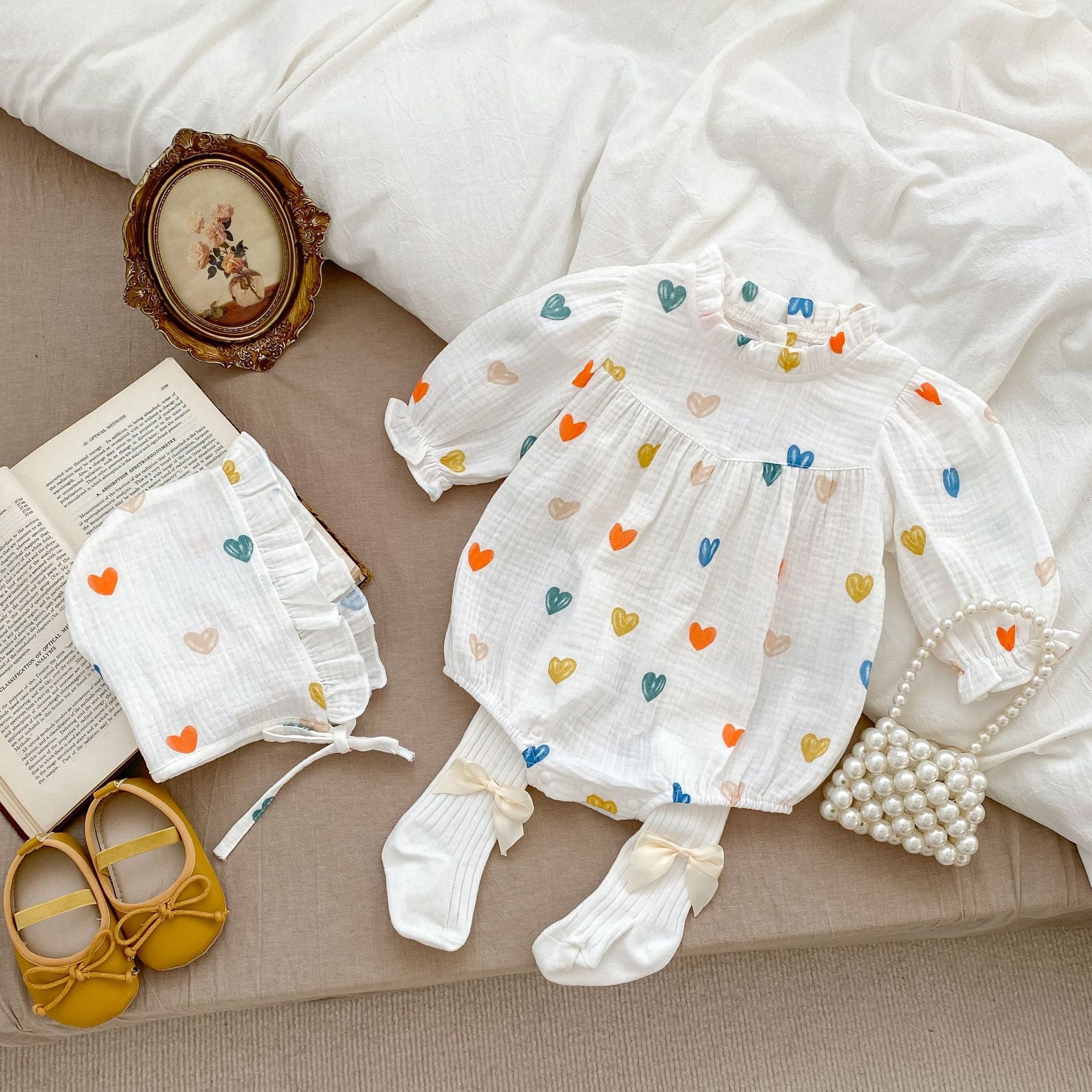 A cute white triangle onesie with heart patterns for baby girls, accompanied by a matching hat, perfect for autumn and spring.