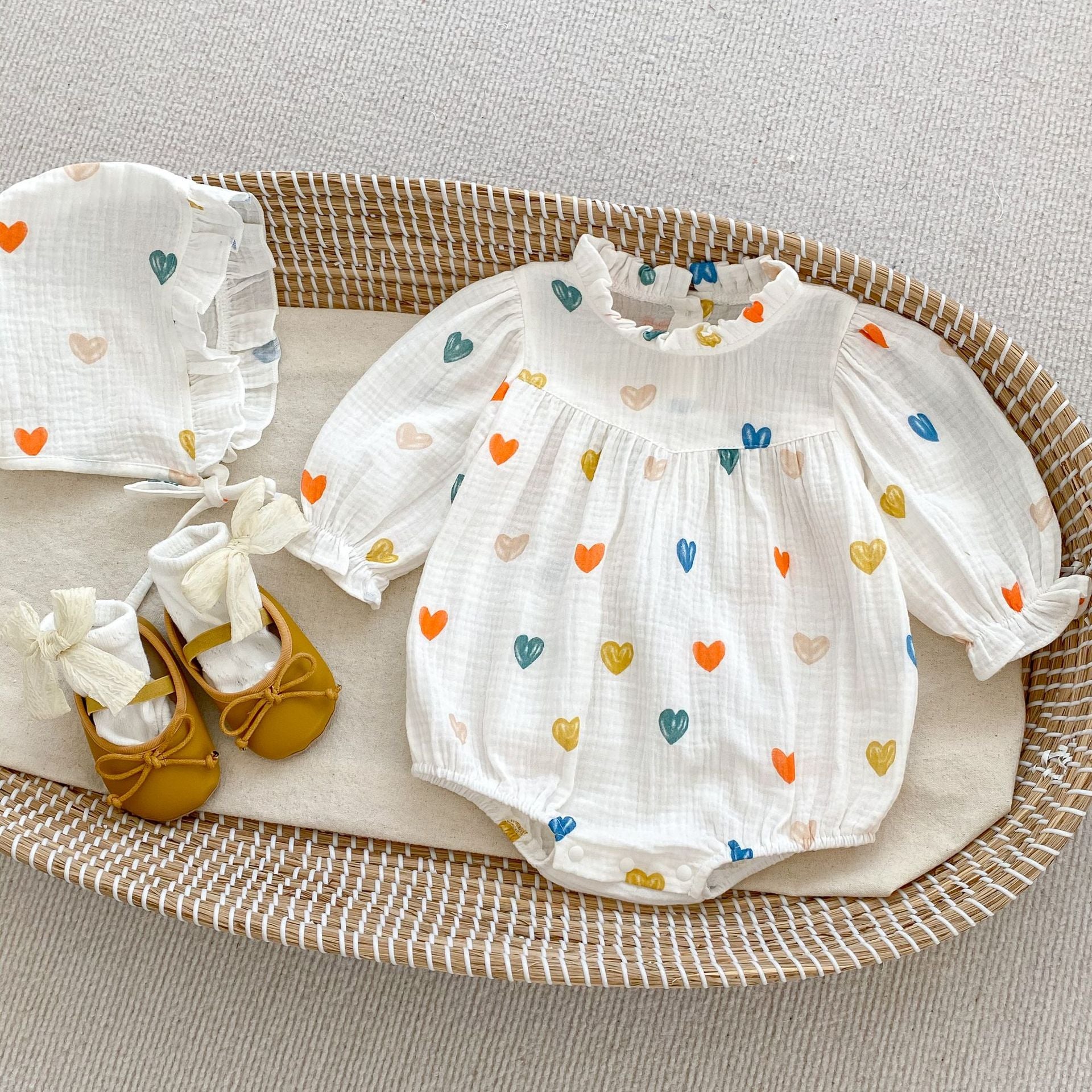 A cute white triangle onesie with heart patterns for baby girls, accompanied by a matching hat, perfect for autumn and spring.