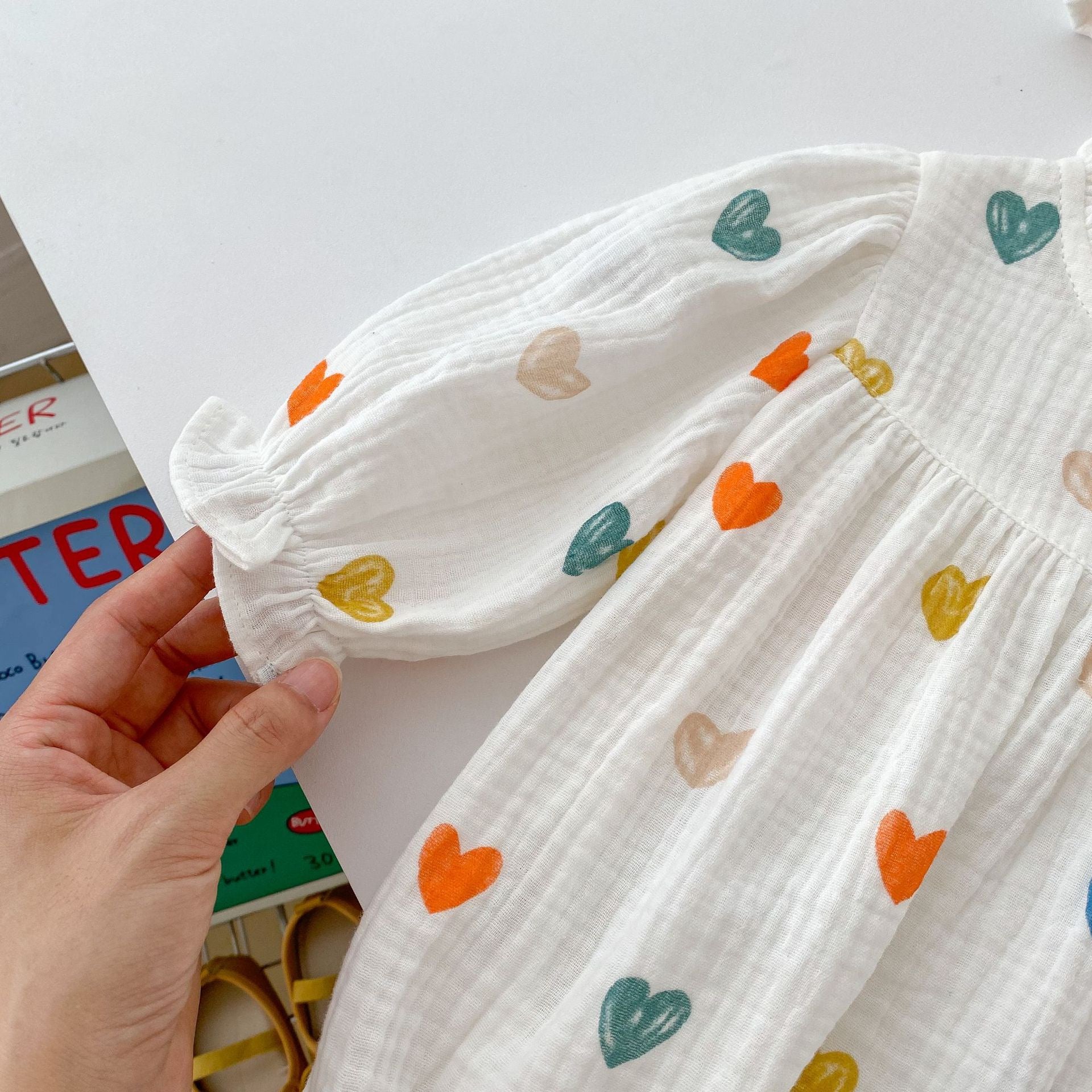 A cute white triangle onesie with heart patterns for baby girls, accompanied by a matching hat, perfect for autumn and spring.