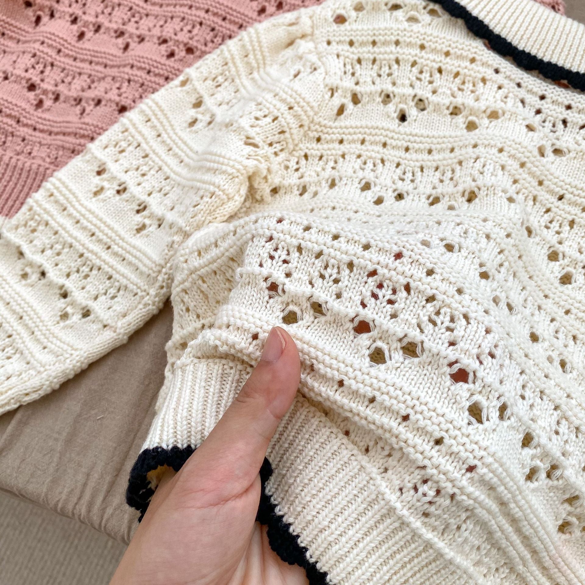 A pink and beige hollow carved design cardigan for baby girls, showcasing its intricate pattern and soft cotton material.